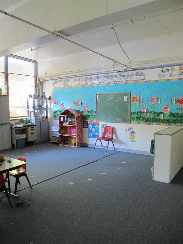 Empty classroom with a chalkboard, bulletin board, and small furniture