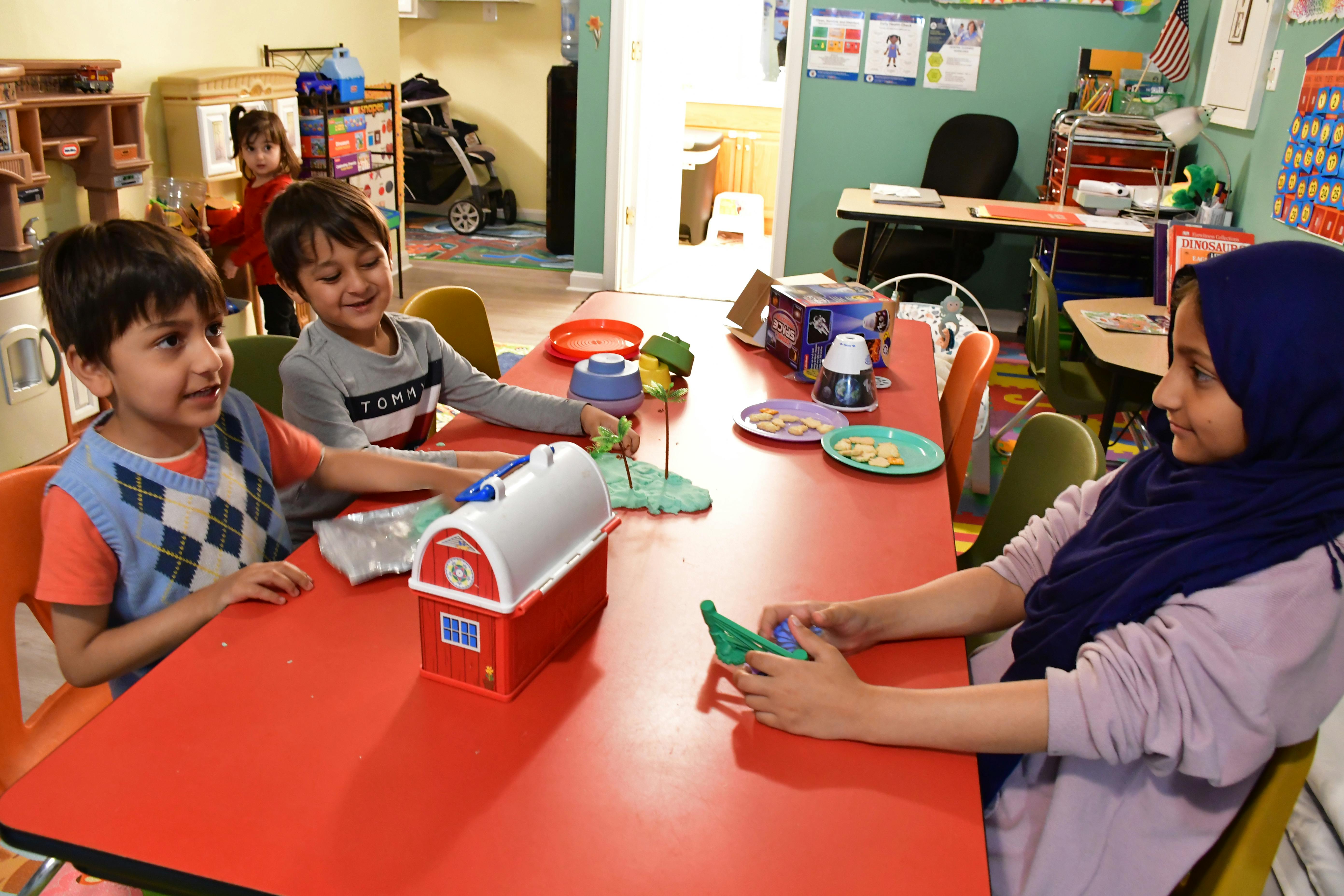Three children playing with toys at a red table in a classroom