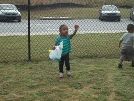 Child holding a plastic container and raising a hand outdoors