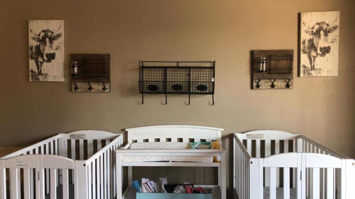 Three white cribs in a row with wall decor above them