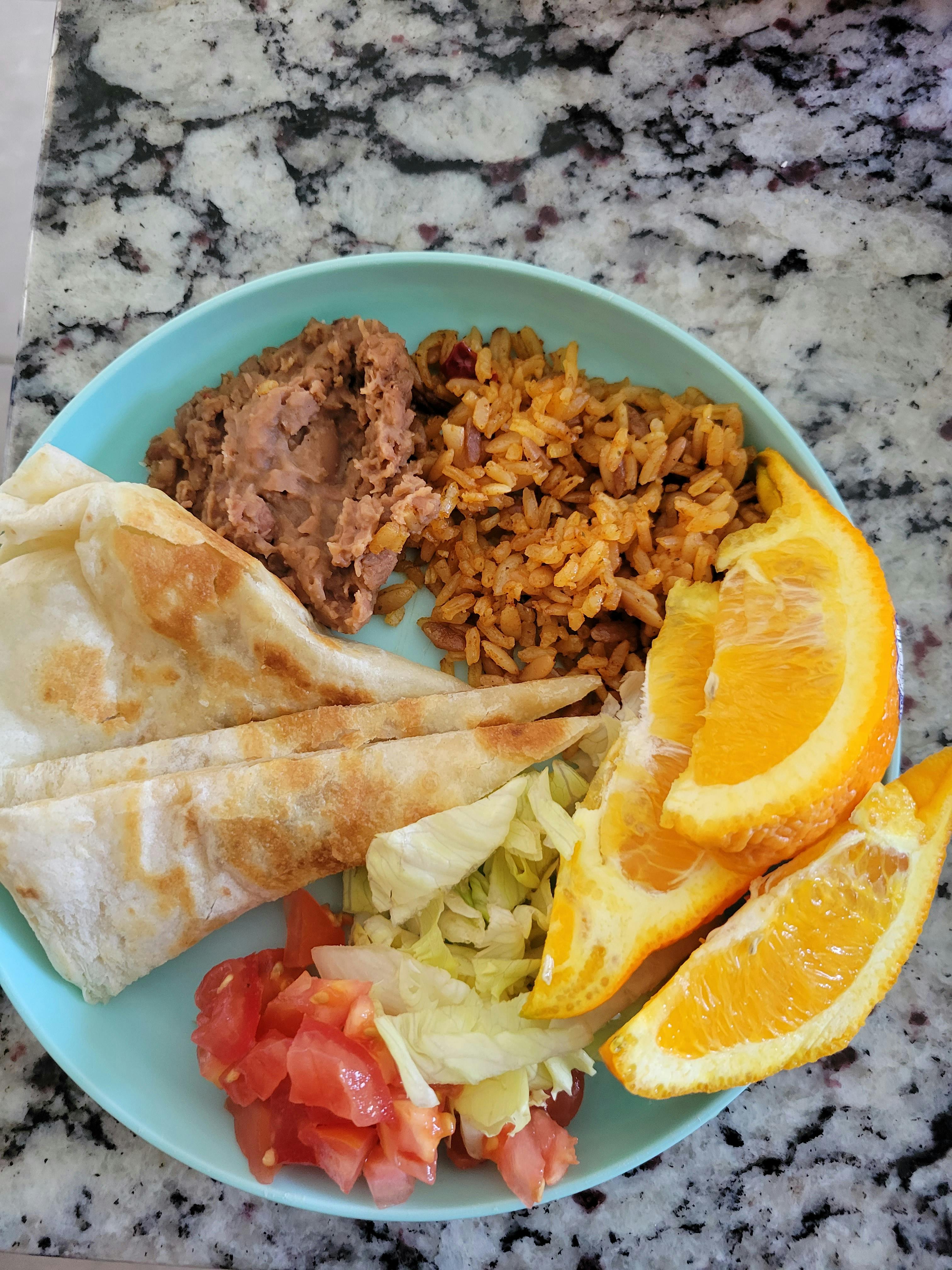 Plate with rice, refried beans, quesadilla slices, salad, and orange wedges