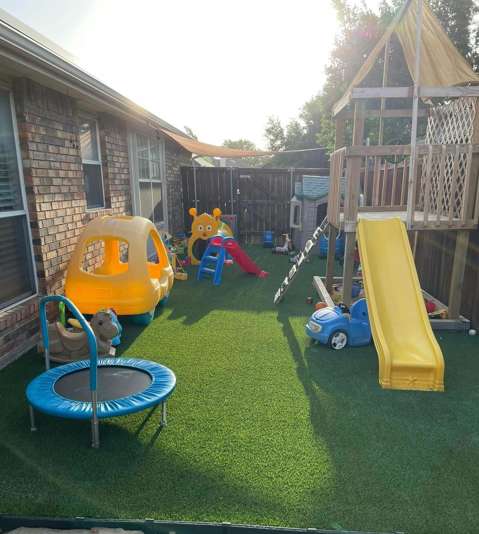 backyard playground with a wooden play structure, yellow slide, toy car, and trampoline