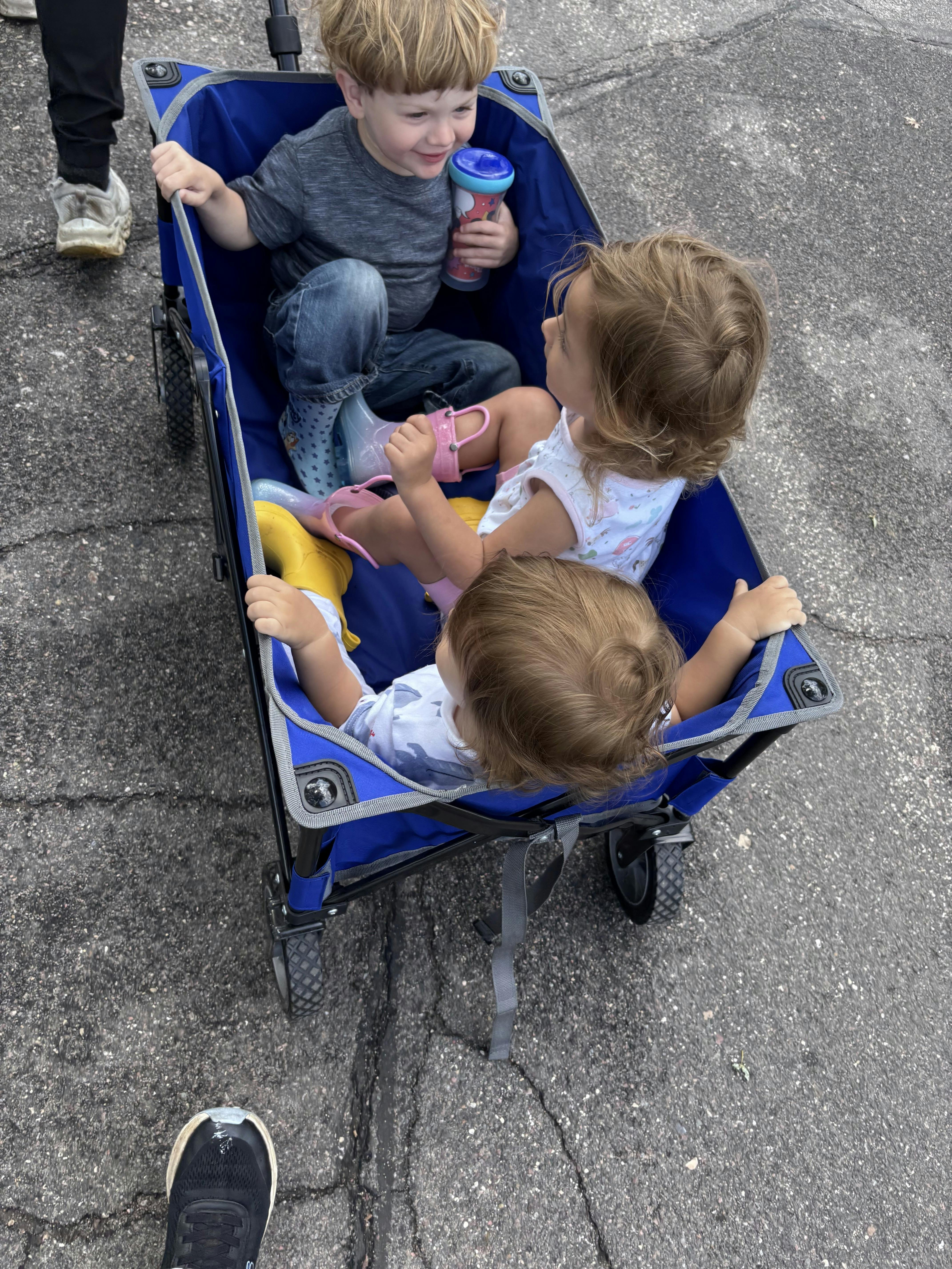 Three children sitting inside a blue wagon on asphalt