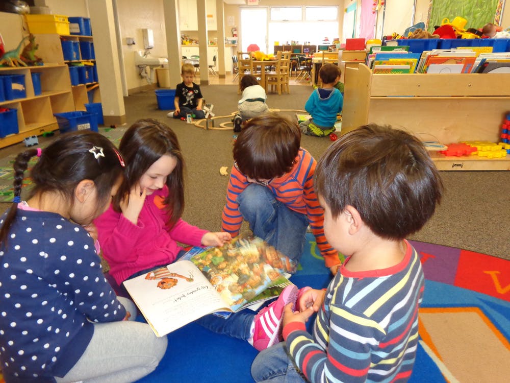 Four children sitting on the floor reading a book together in a classroom