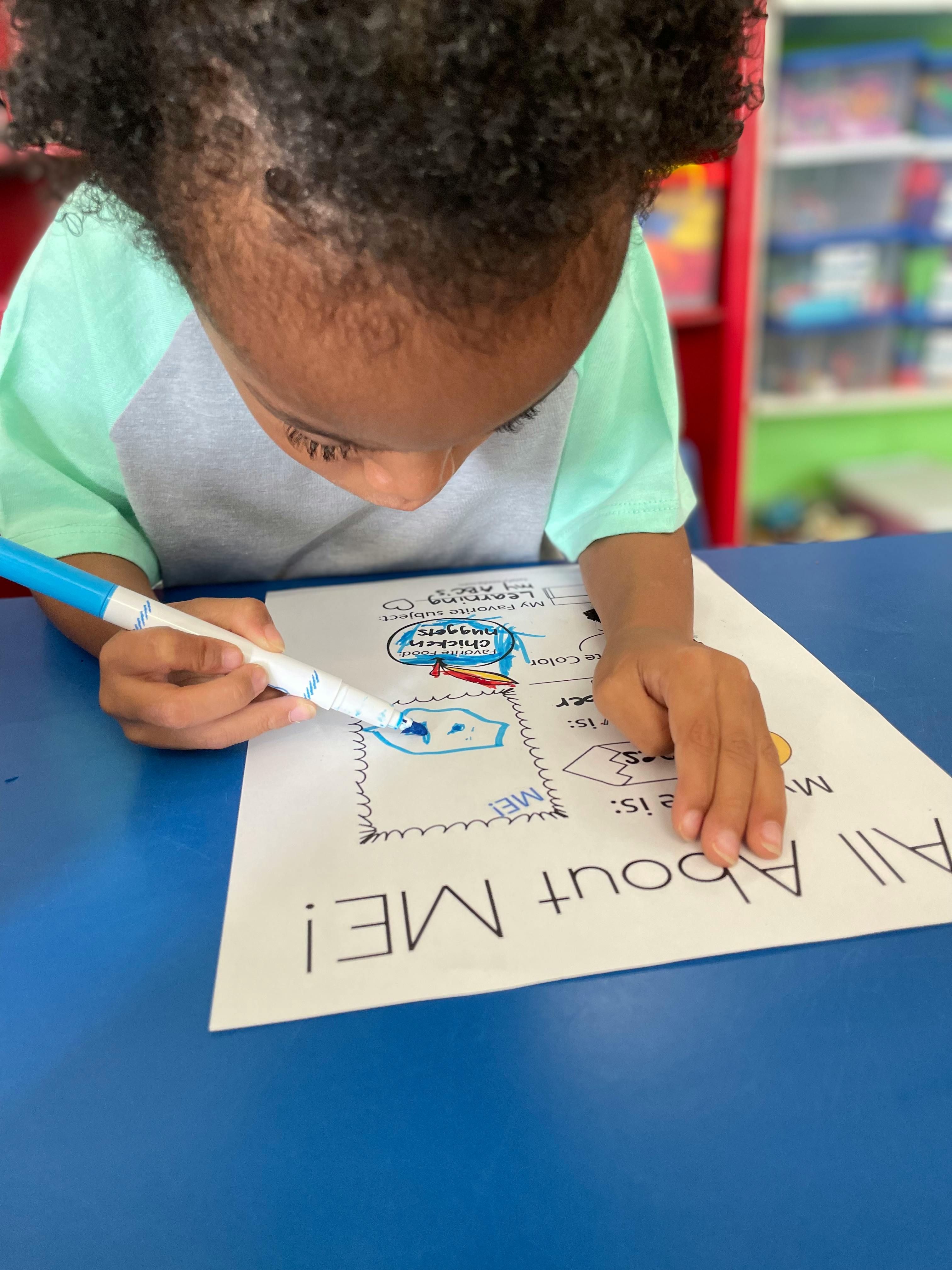 Child coloring on a paper with a blue marker