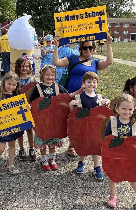 Adult and children with "St. Mary's School" signs and apple costumes