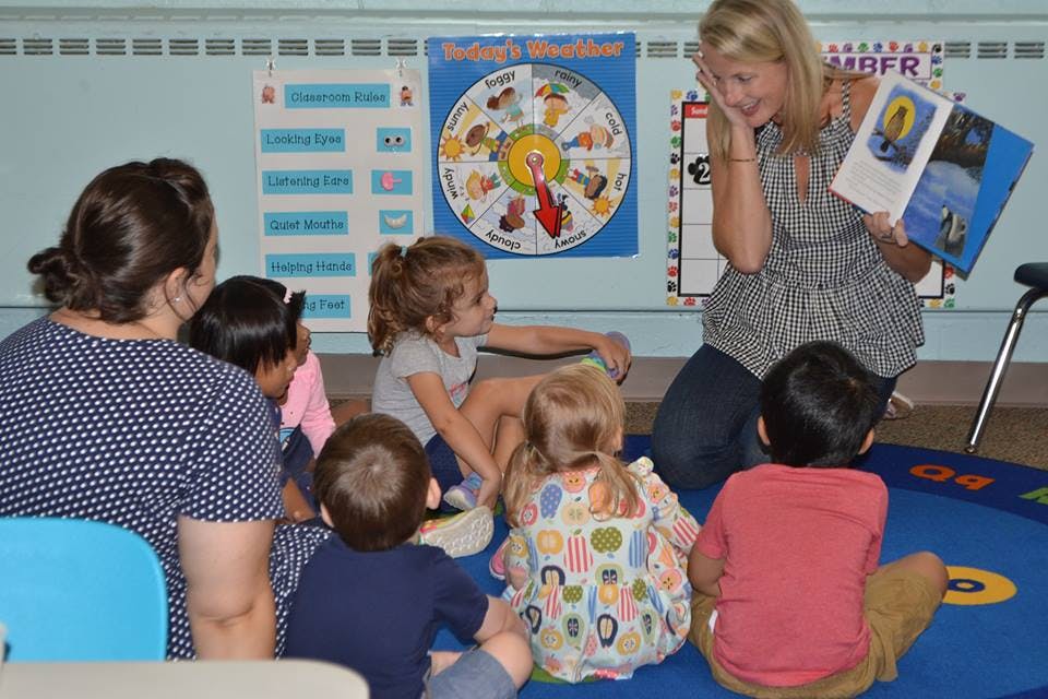 Adult reading a book to a group of children in a classroom