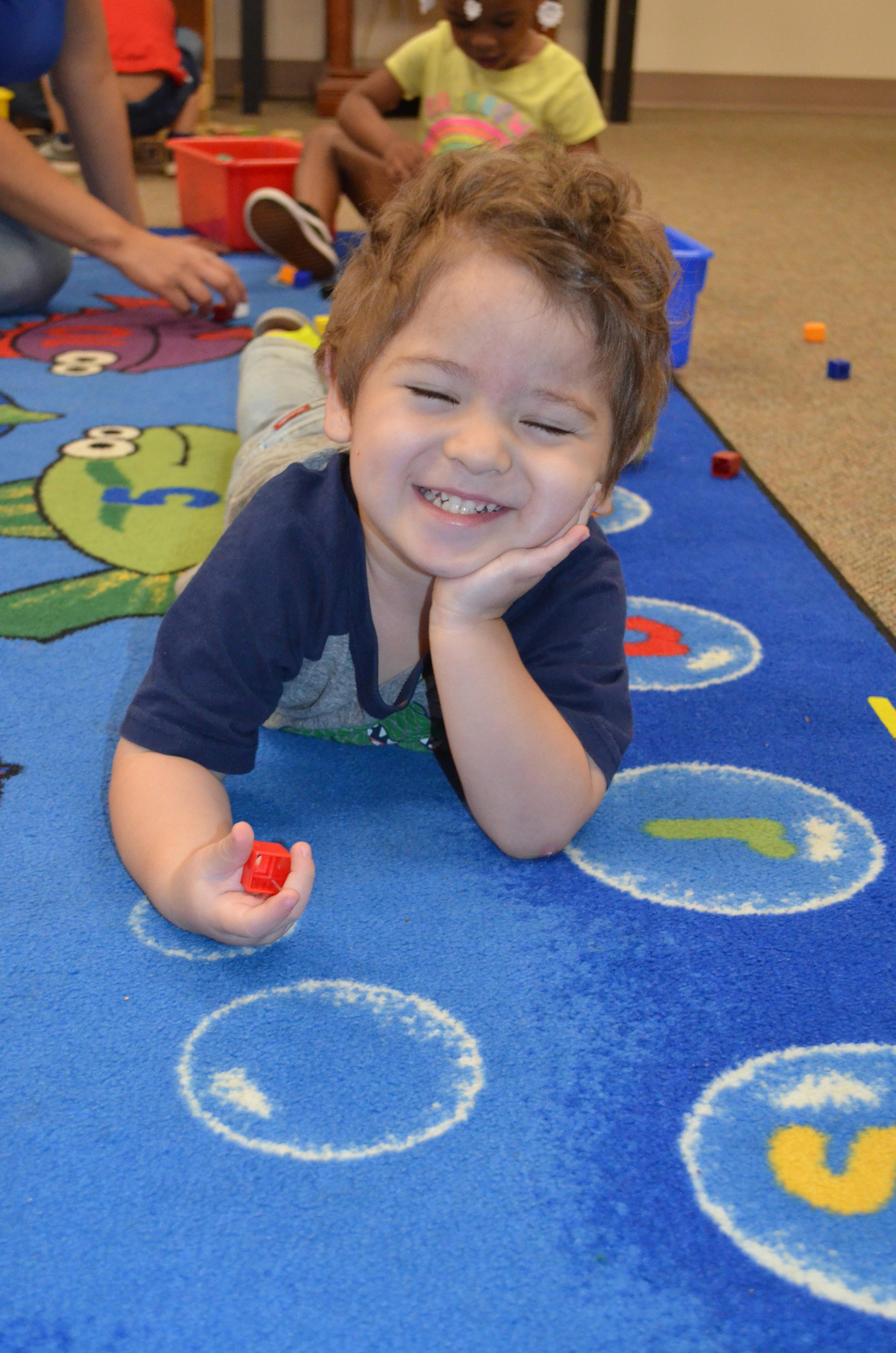 Child lying on a blue rug, holding a red block