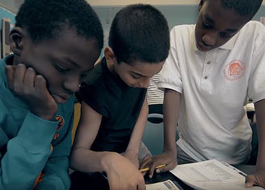 Three children looking at papers in a classroom