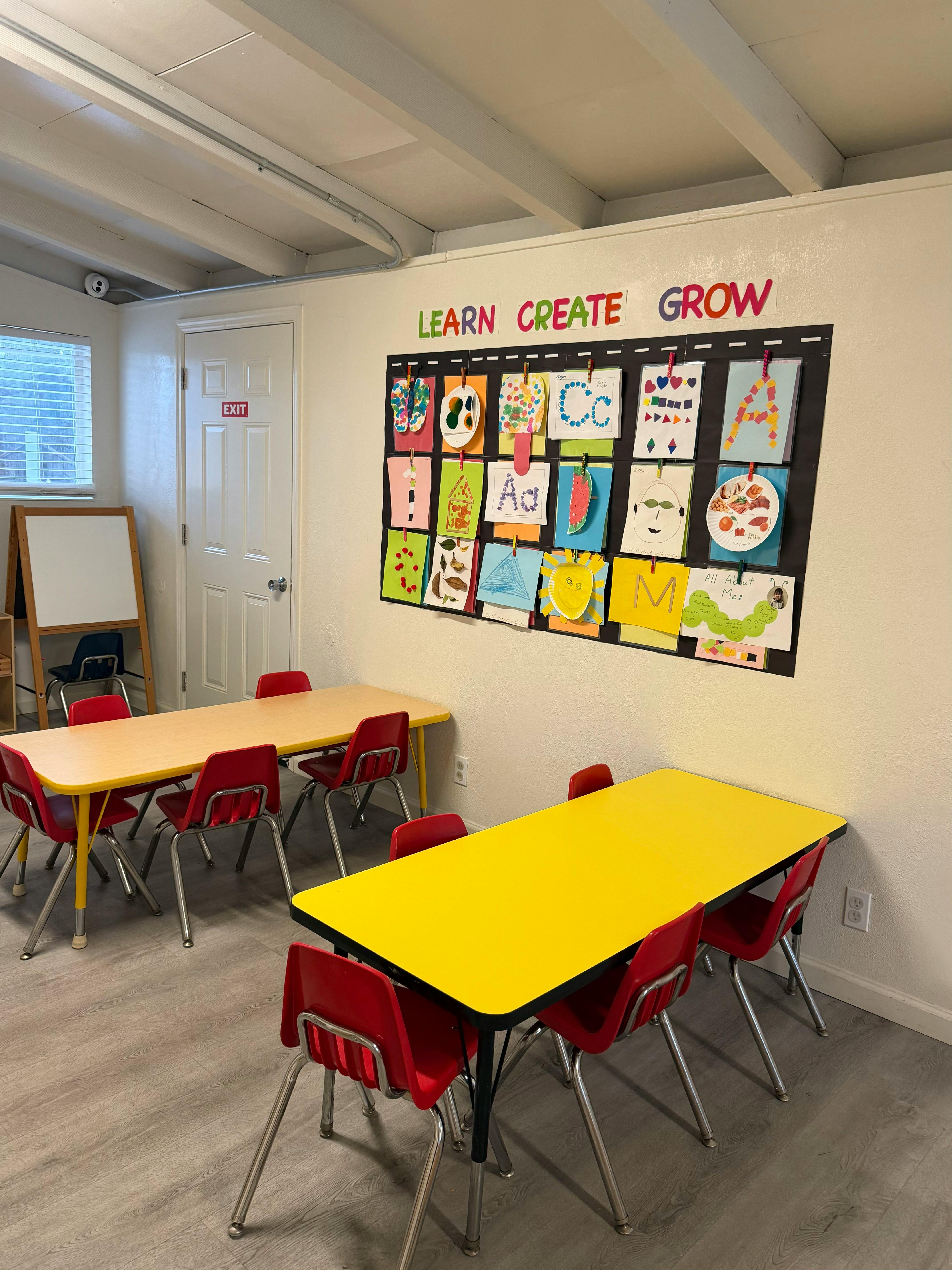 Classroom with yellow tables, red chairs, and children's artwork on the wall