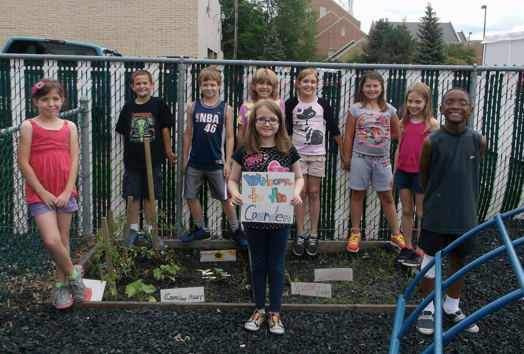 Group of children standing in front of a fence, one child holding a sign