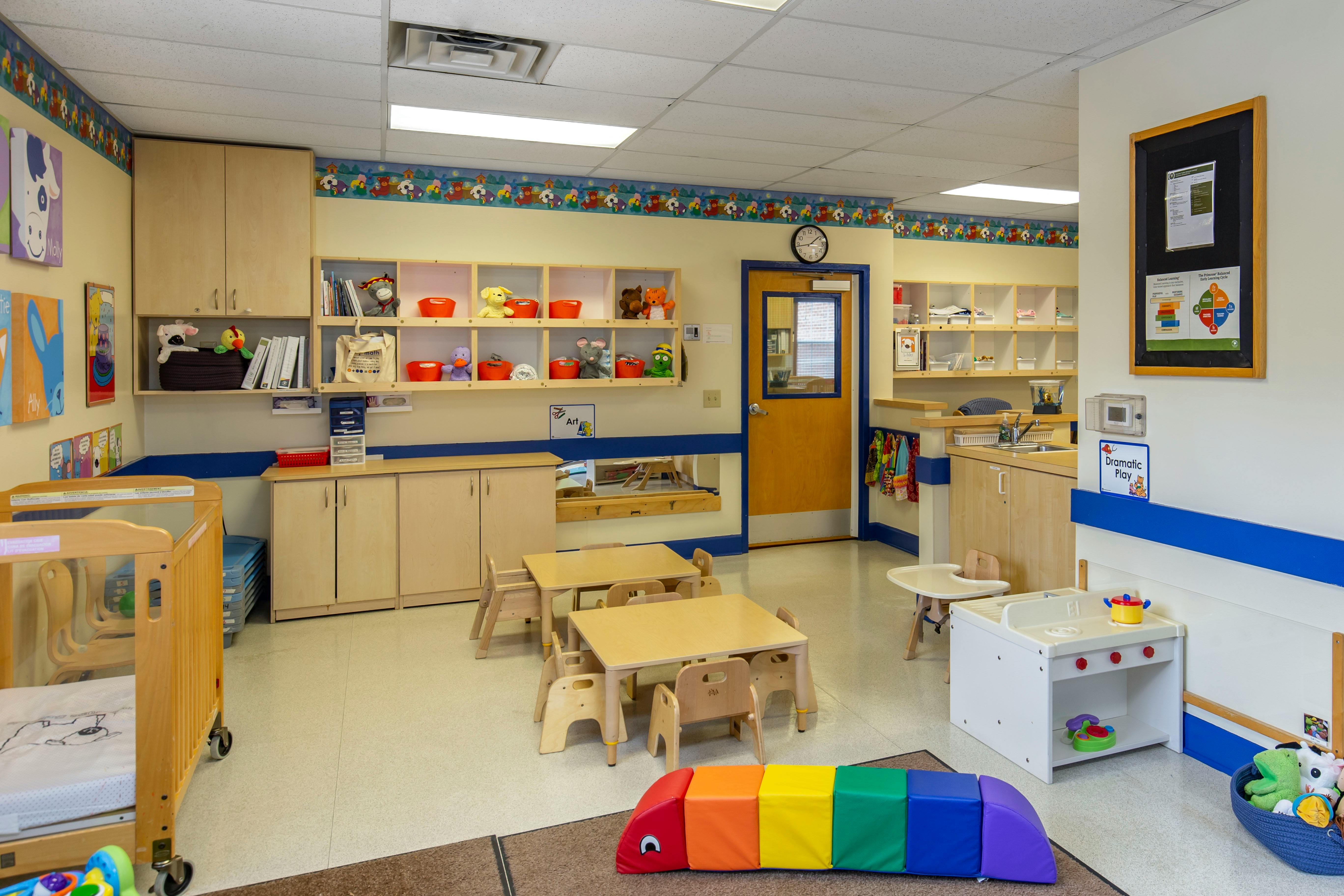 Classroom with crib, tables, shelves with toys, and play kitchen