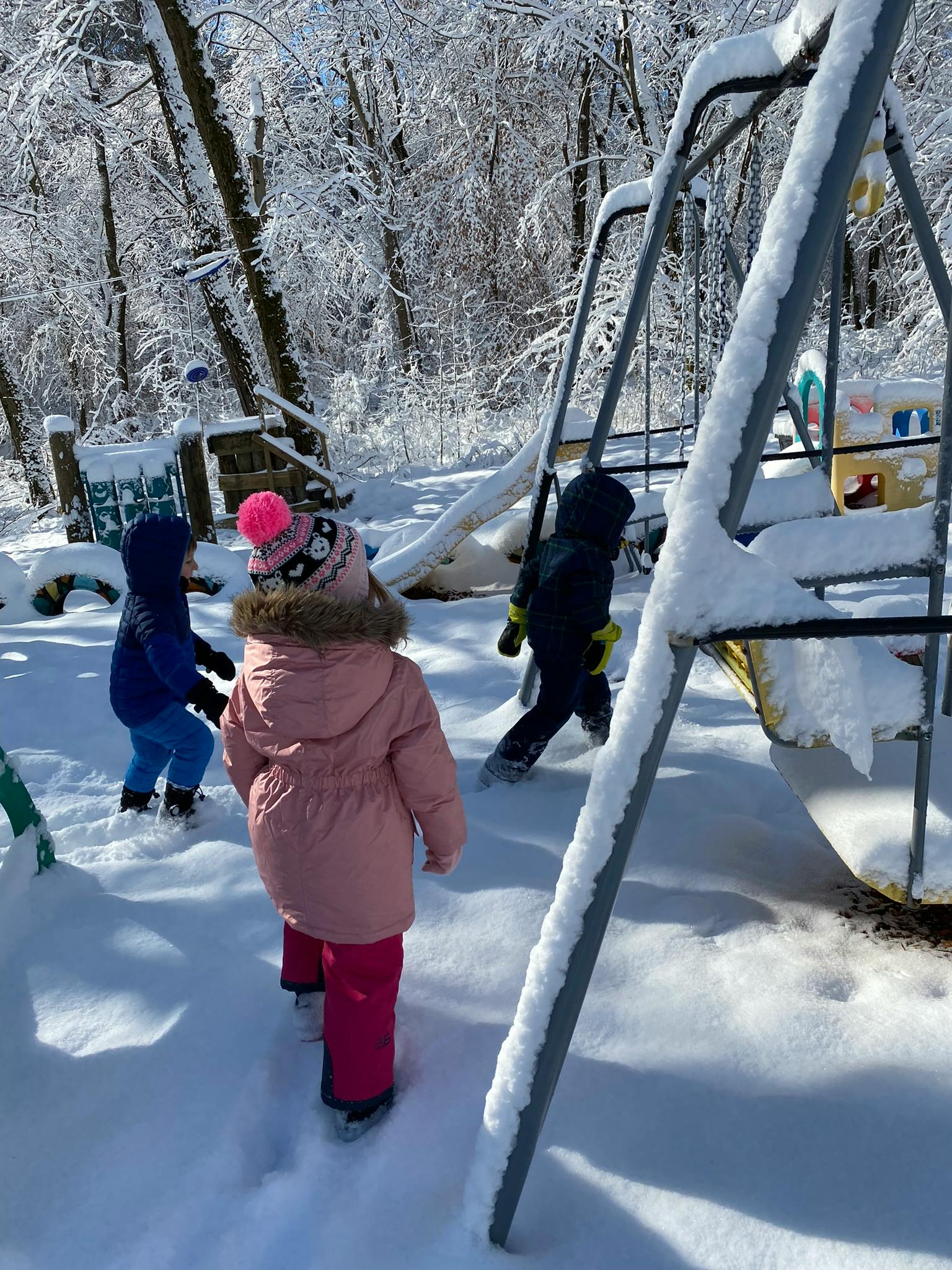 Three children walking in snow near a playground