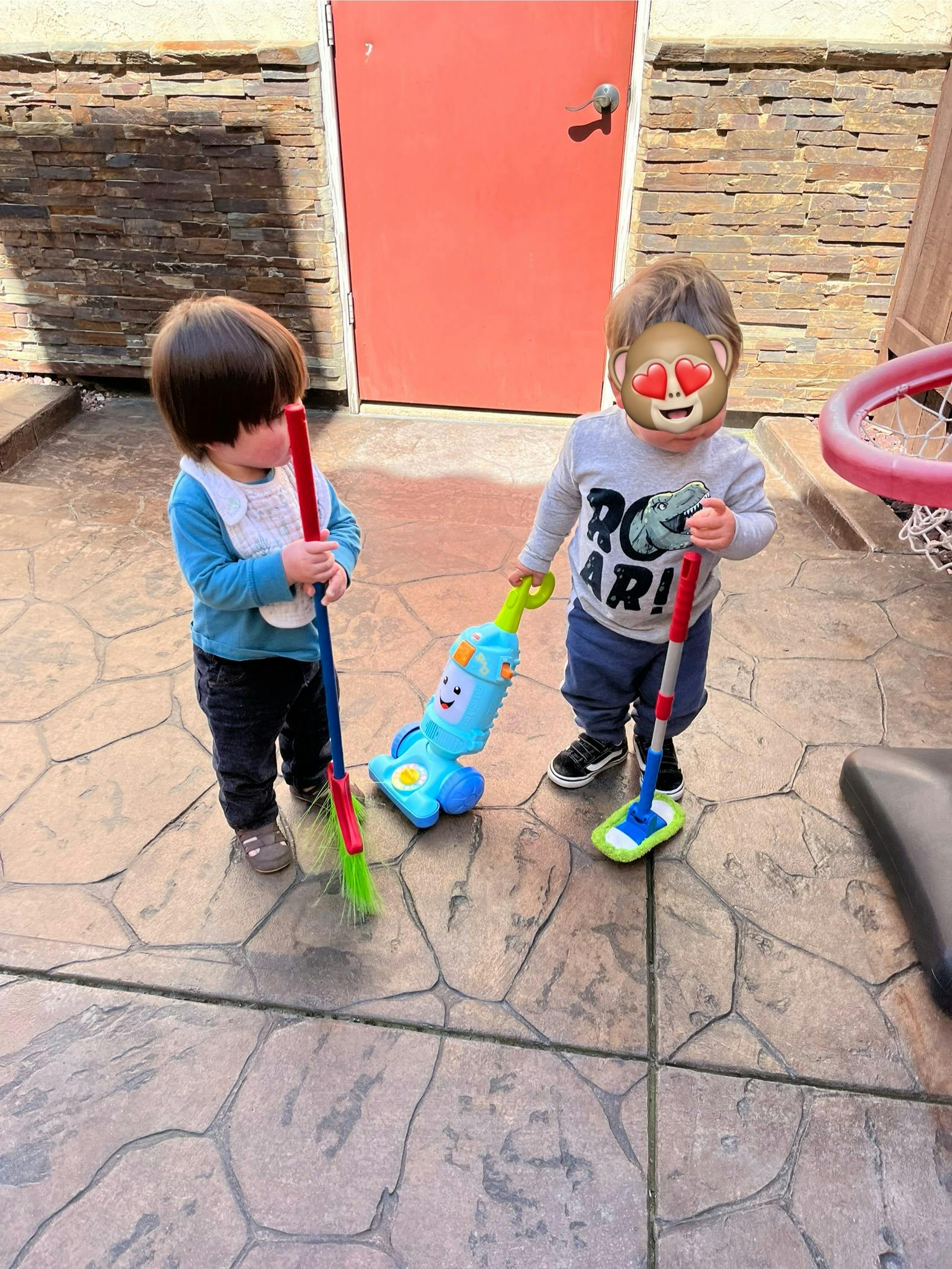 Two children playing with toy cleaning tools on a patio