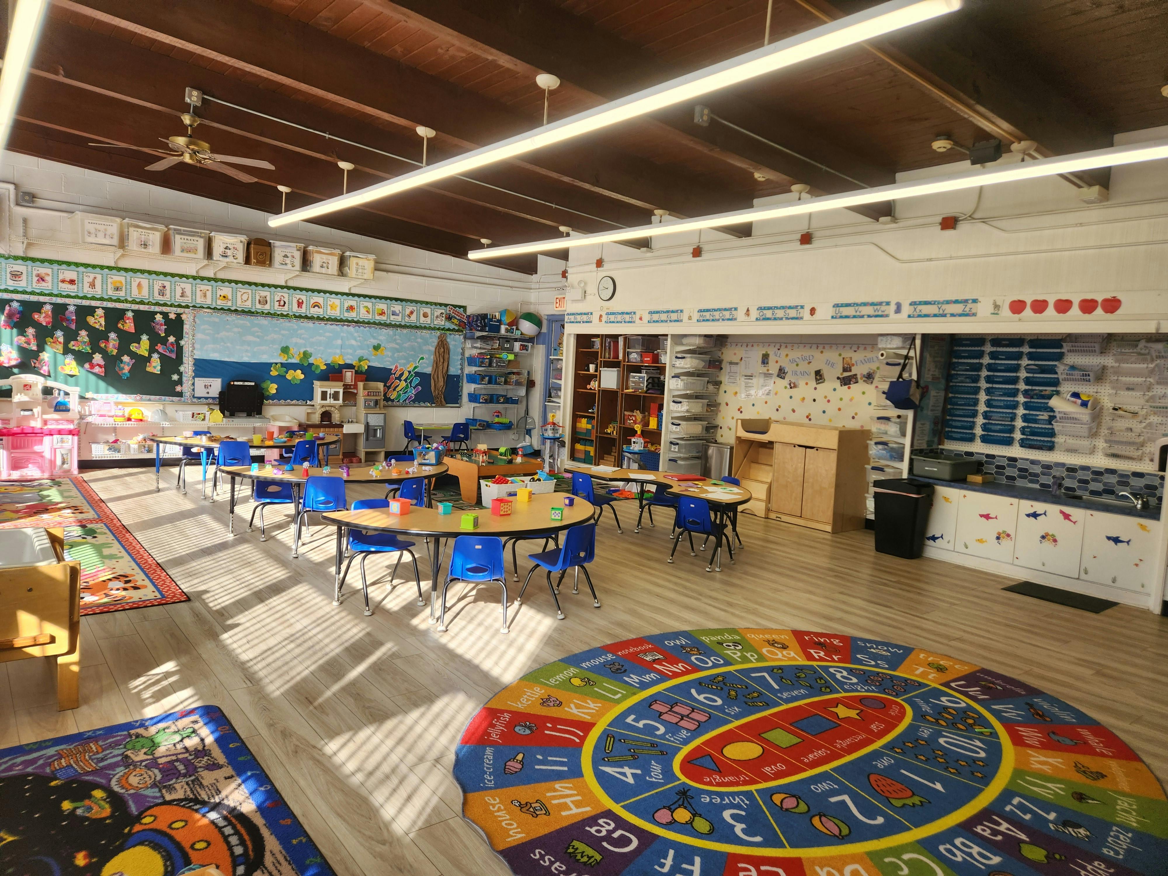 Empty classroom with small tables and chairs, colorful rugs on the floor