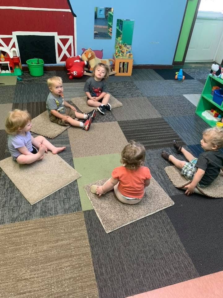 Four children sitting on carpet squares in a playroom