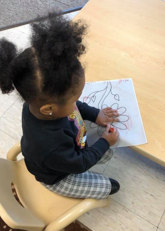 Child coloring a drawing of a flower and leaves