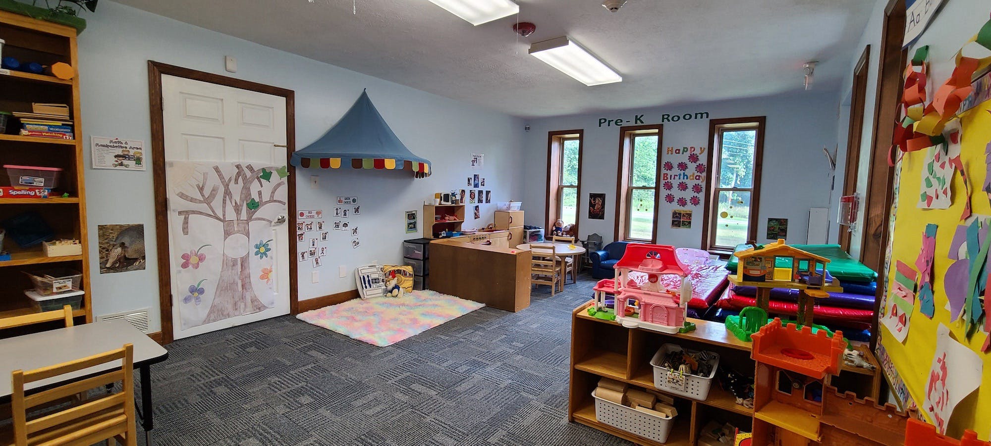 Pre-K classroom with various play areas, a colorful rug, and windows