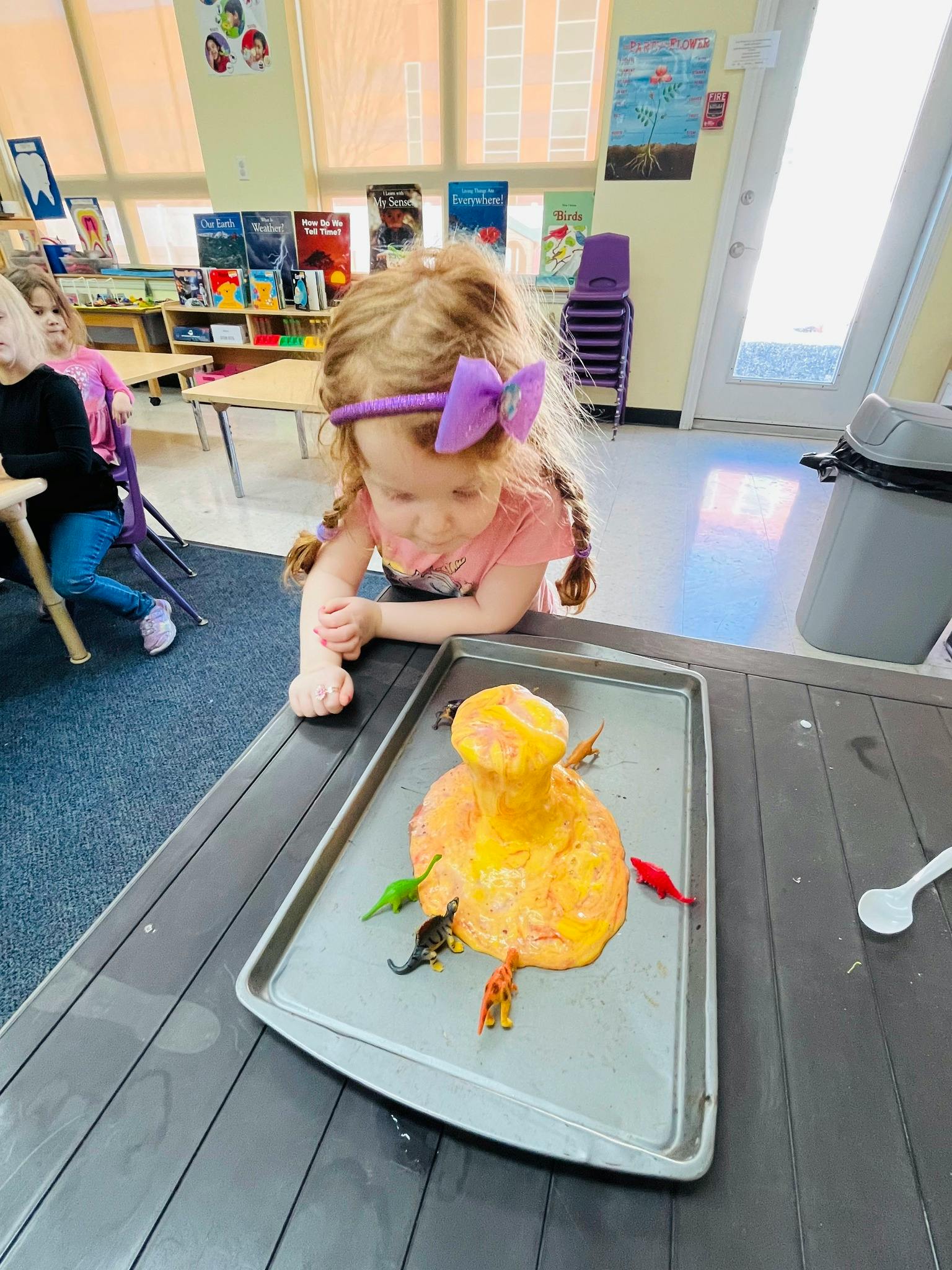 Child looking at a volcano science experiment with toy dinosaurs