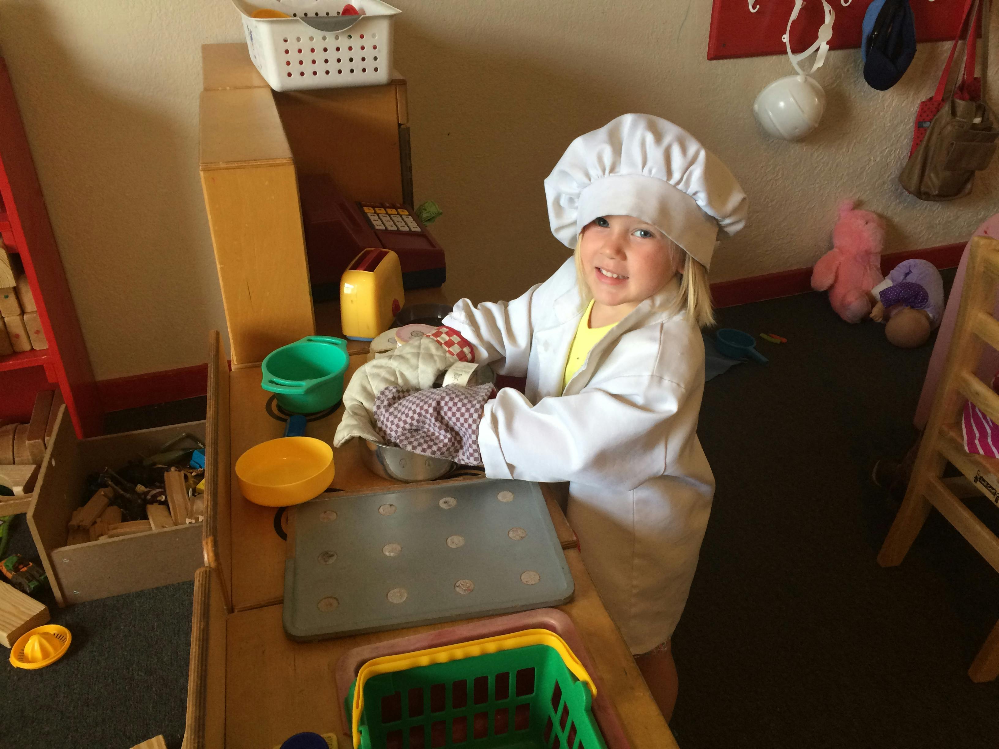 Child in chef's hat and coat playing with toy kitchen items