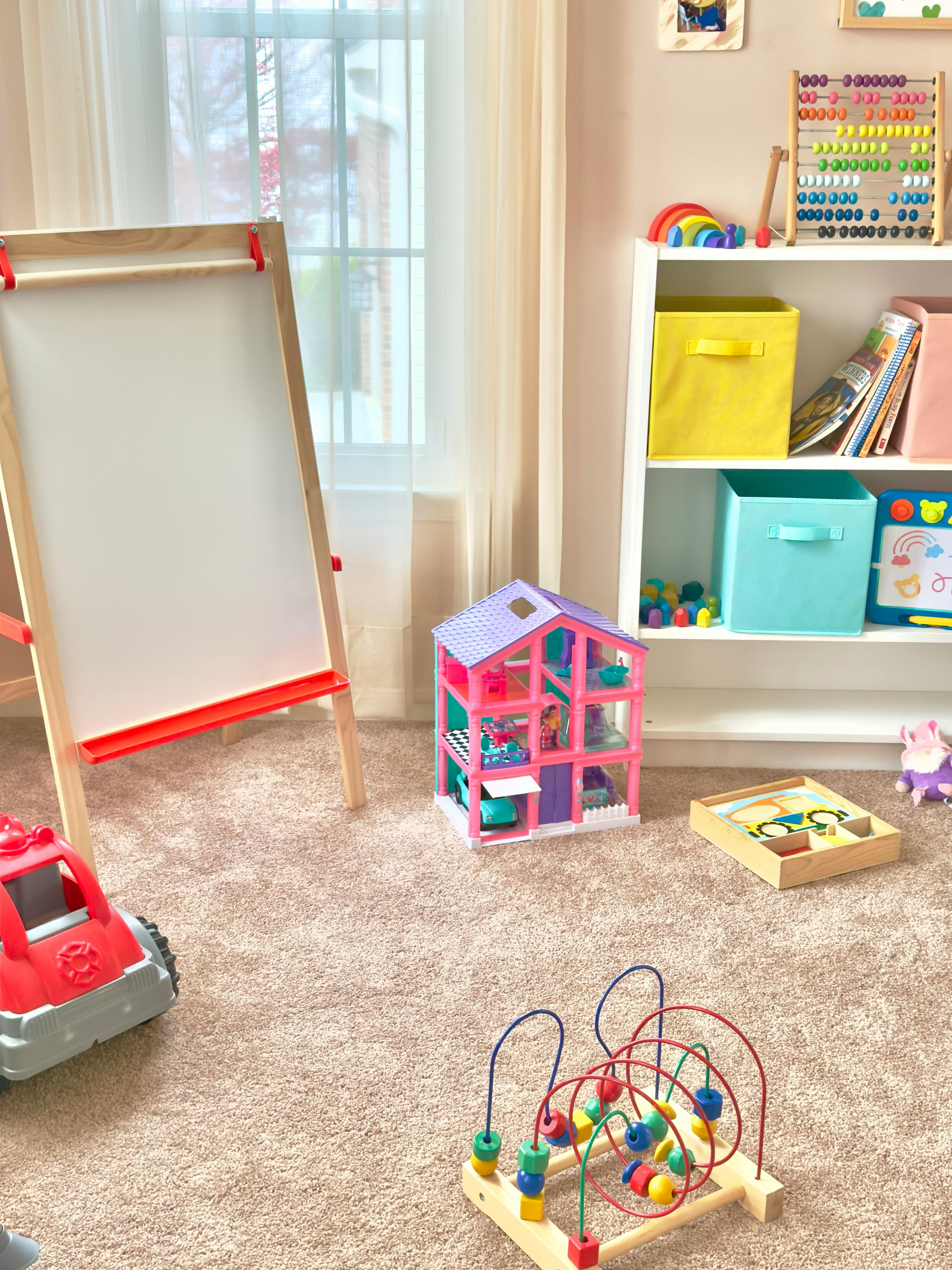 Playroom with an easel, dollhouse, and various toys on the floor