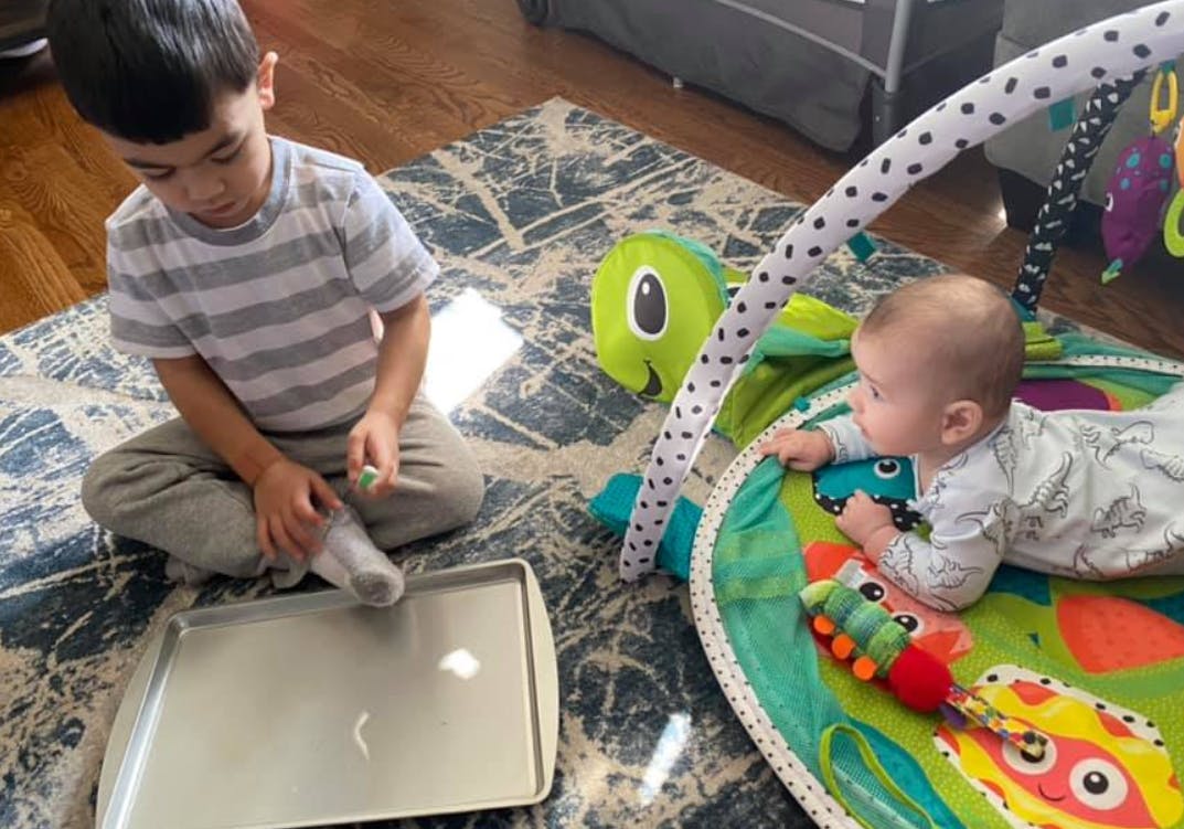 Child sitting on rug next to baby on playmat