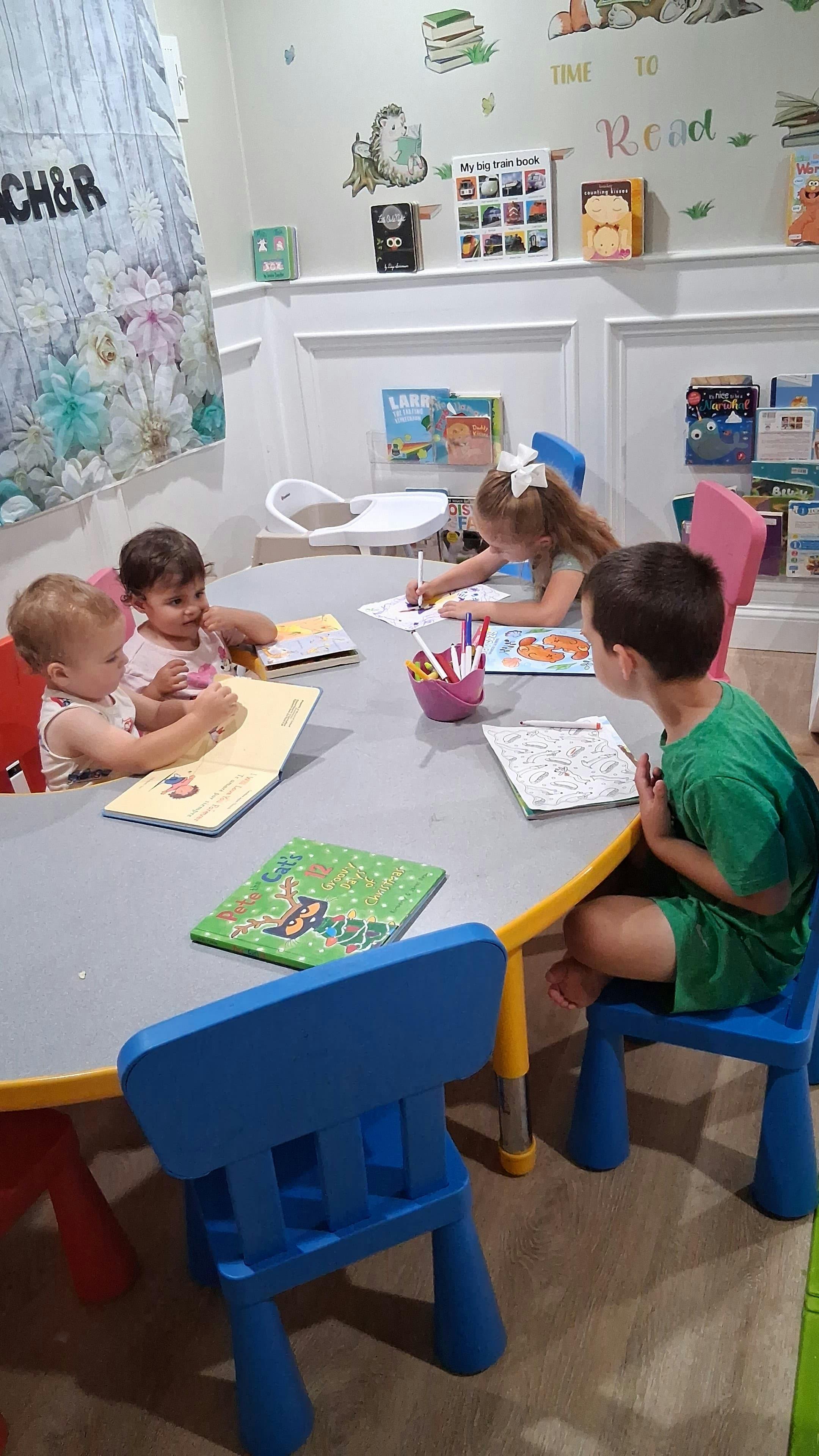 Four children sitting at a table reading and drawing in a classroom