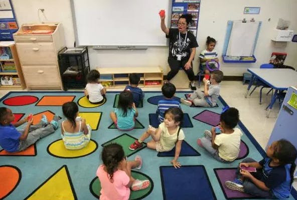 Adult and children sitting on a colorful rug in a classroom