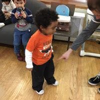 Toddler in orange shirt looking at a pointing hand