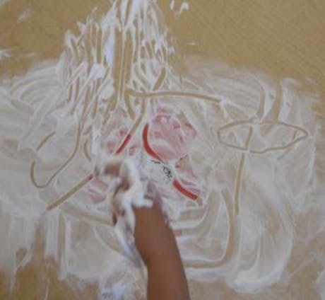 Child's arm and hand covered in white foam, drawing on a surface