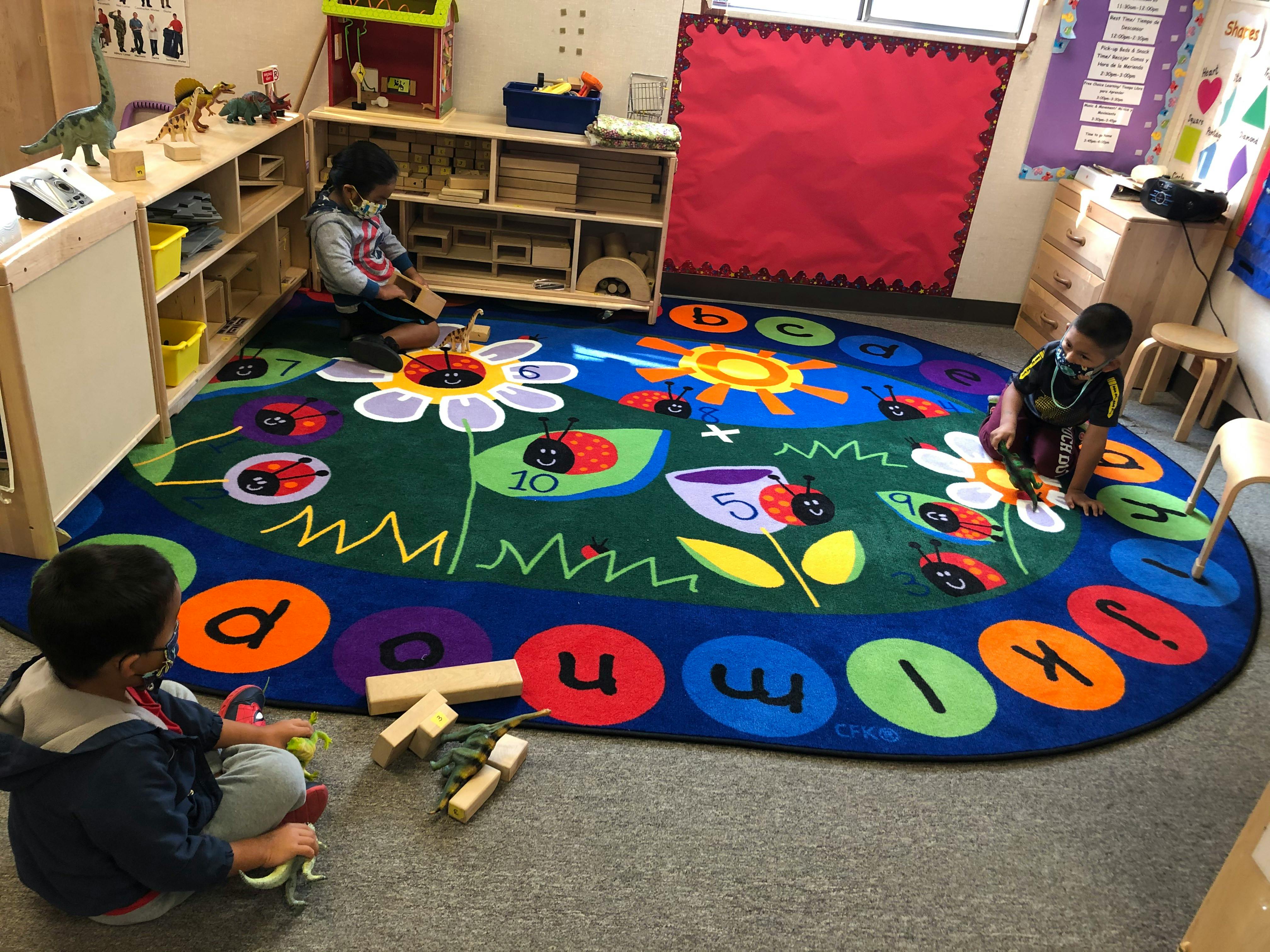 Three children playing on a colorful rug in a classroom