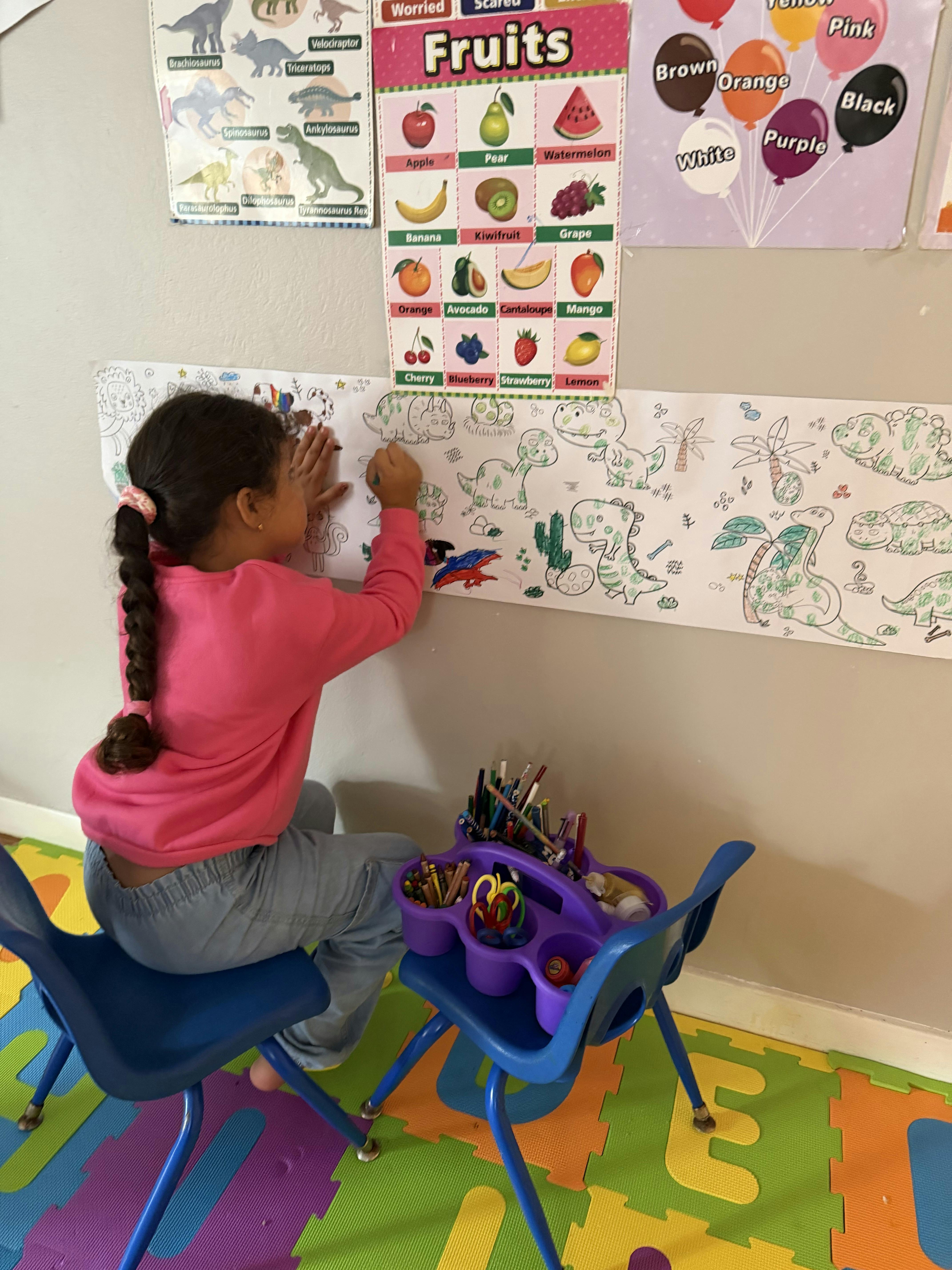 Child coloring a long dinosaur illustration on a wall