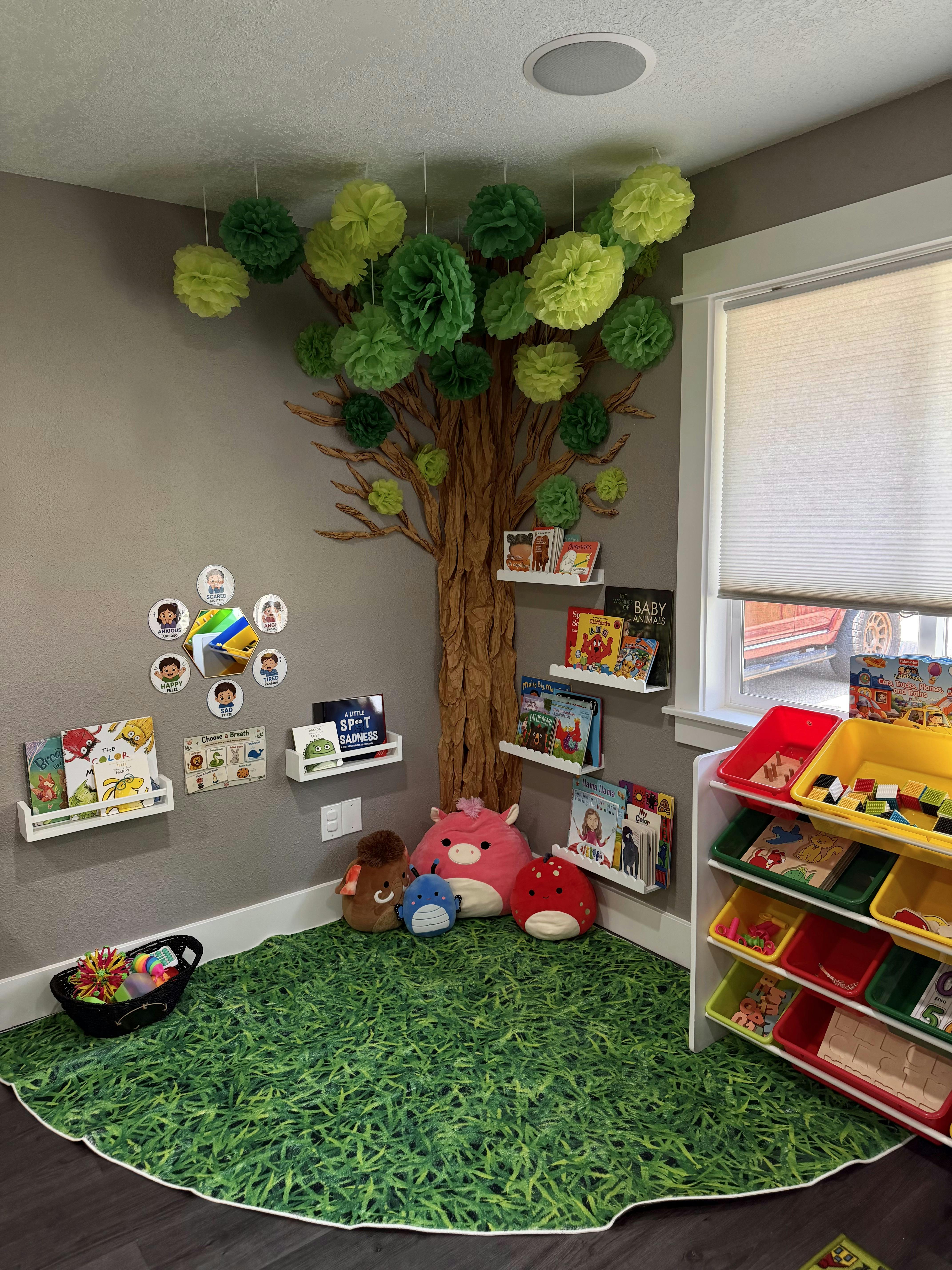 A child reading corner with a tree decoration, bookshelves, and grass-style rug