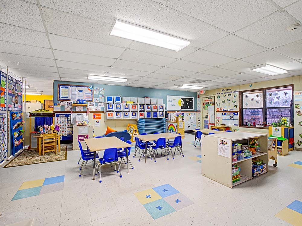 Empty classroom with small tables and chairs, and play areas