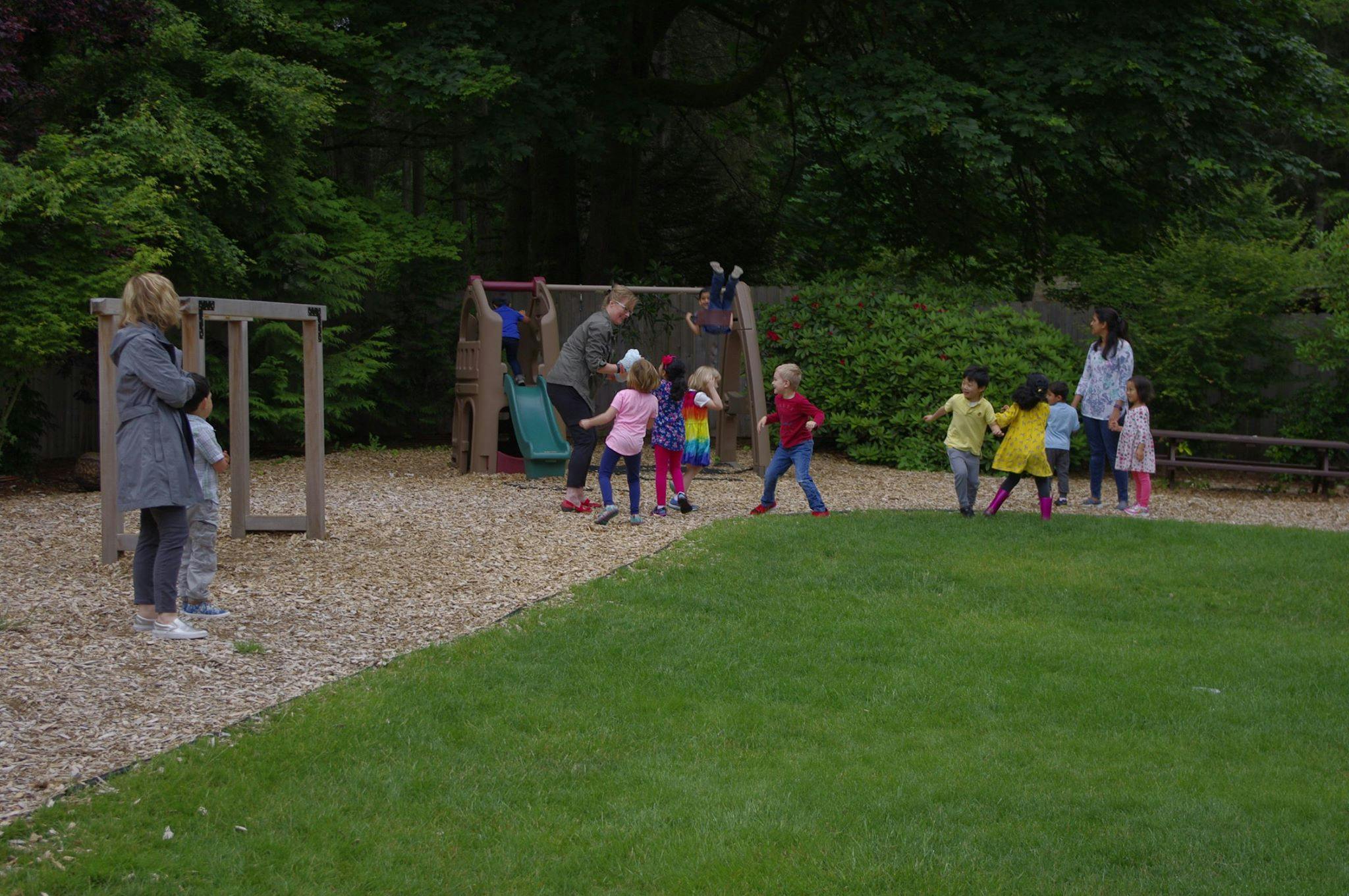 Adults and children playing on a playground with wood chips and grass