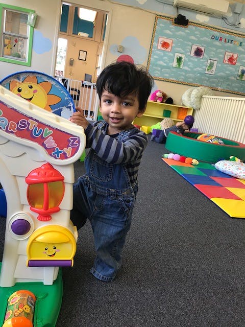 Child in overalls standing next to a colorful toy in a play area