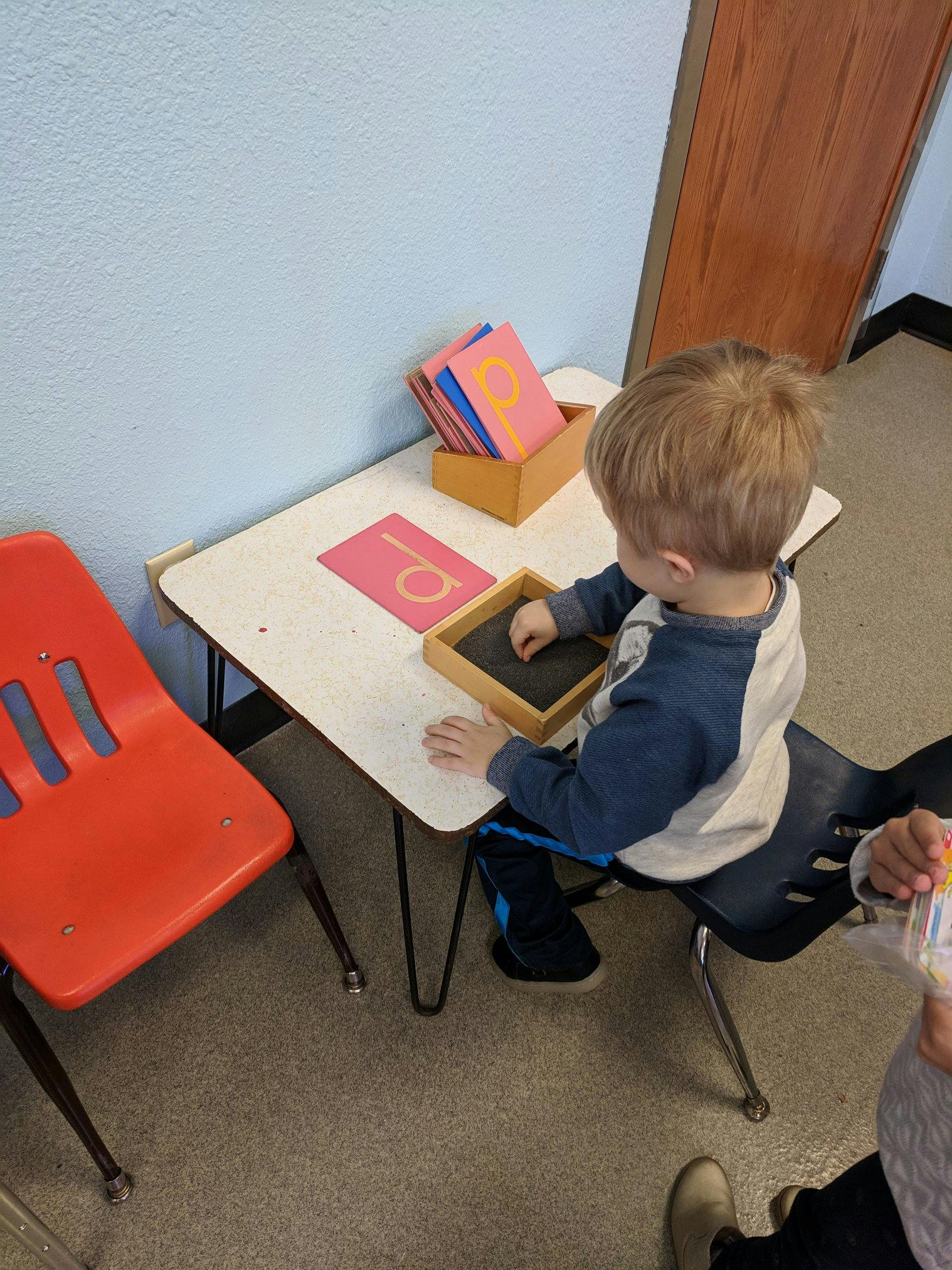 Child sitting at a table, tracing a letter on a learning board