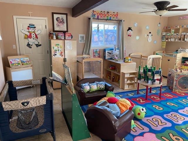 A room with a playpen, small chairs, and a colorful alphabet rug