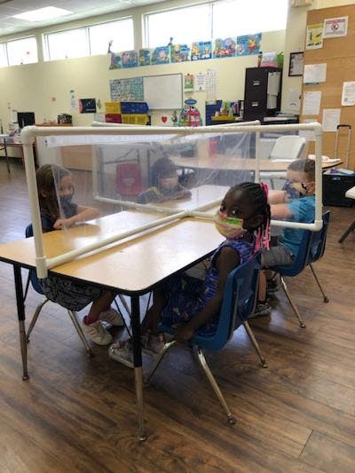 Children sitting at desks with clear dividers in a classroom
