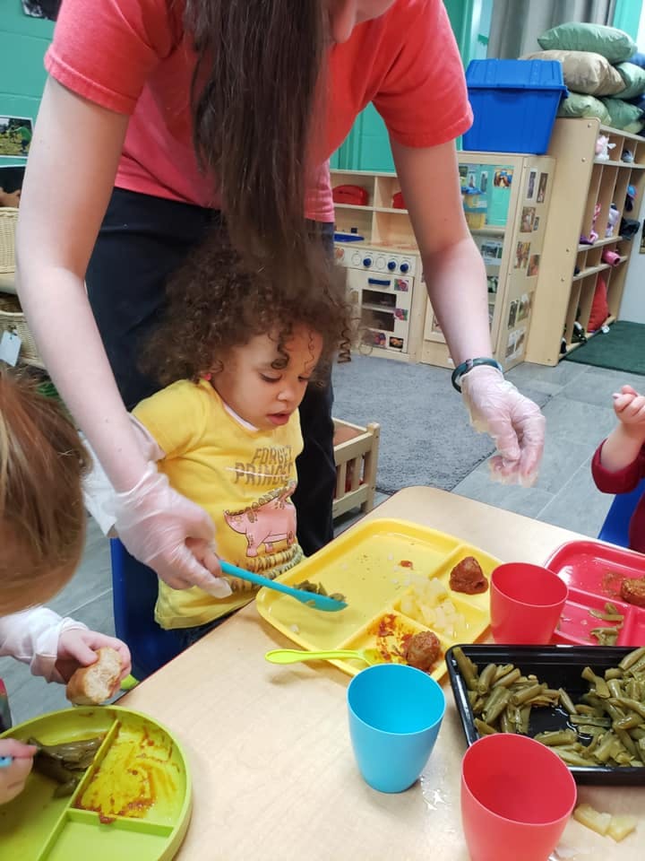 Adult helping a child with a meal on a tray