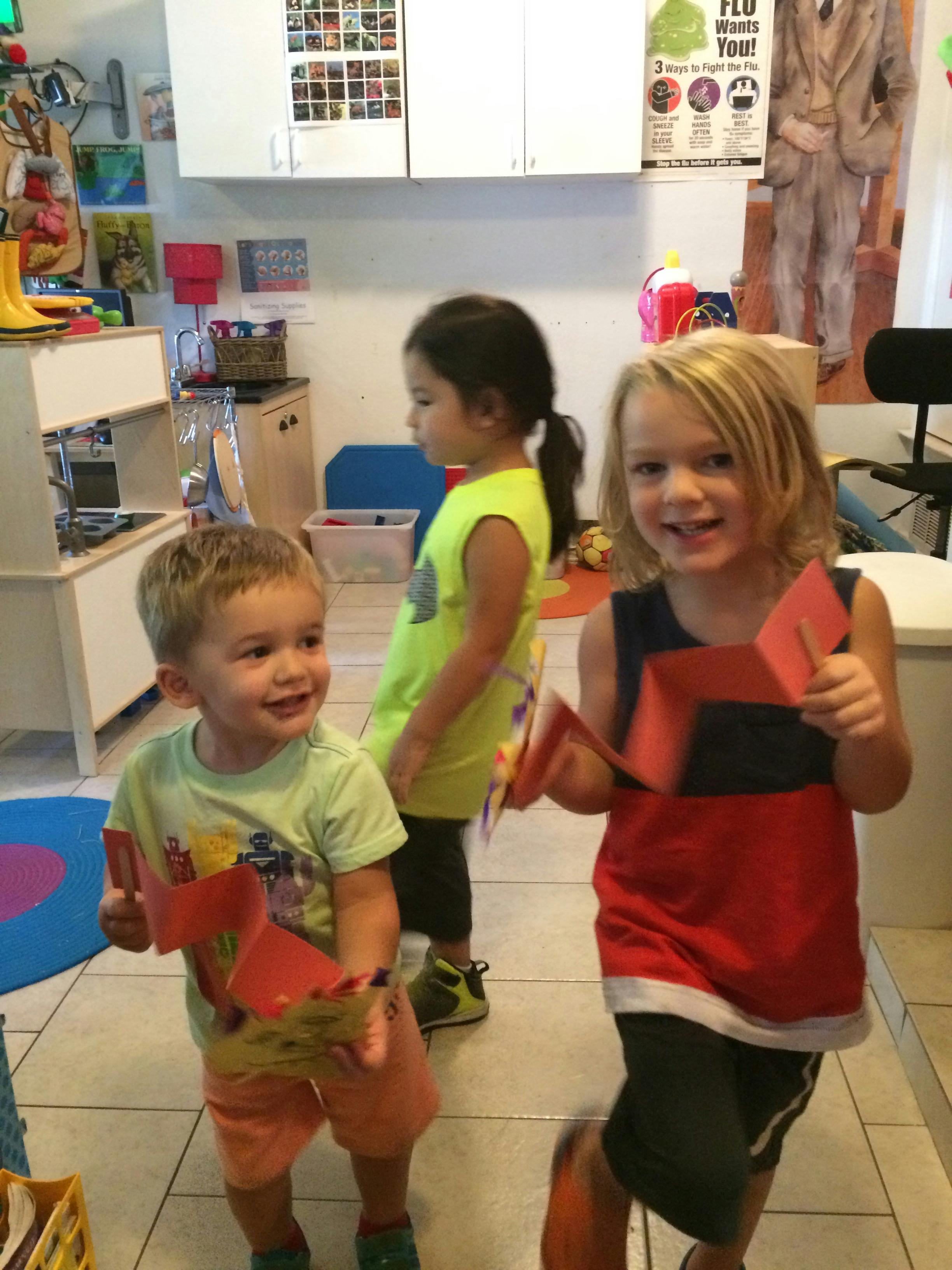 Three children holding red paper crafts in a classroom