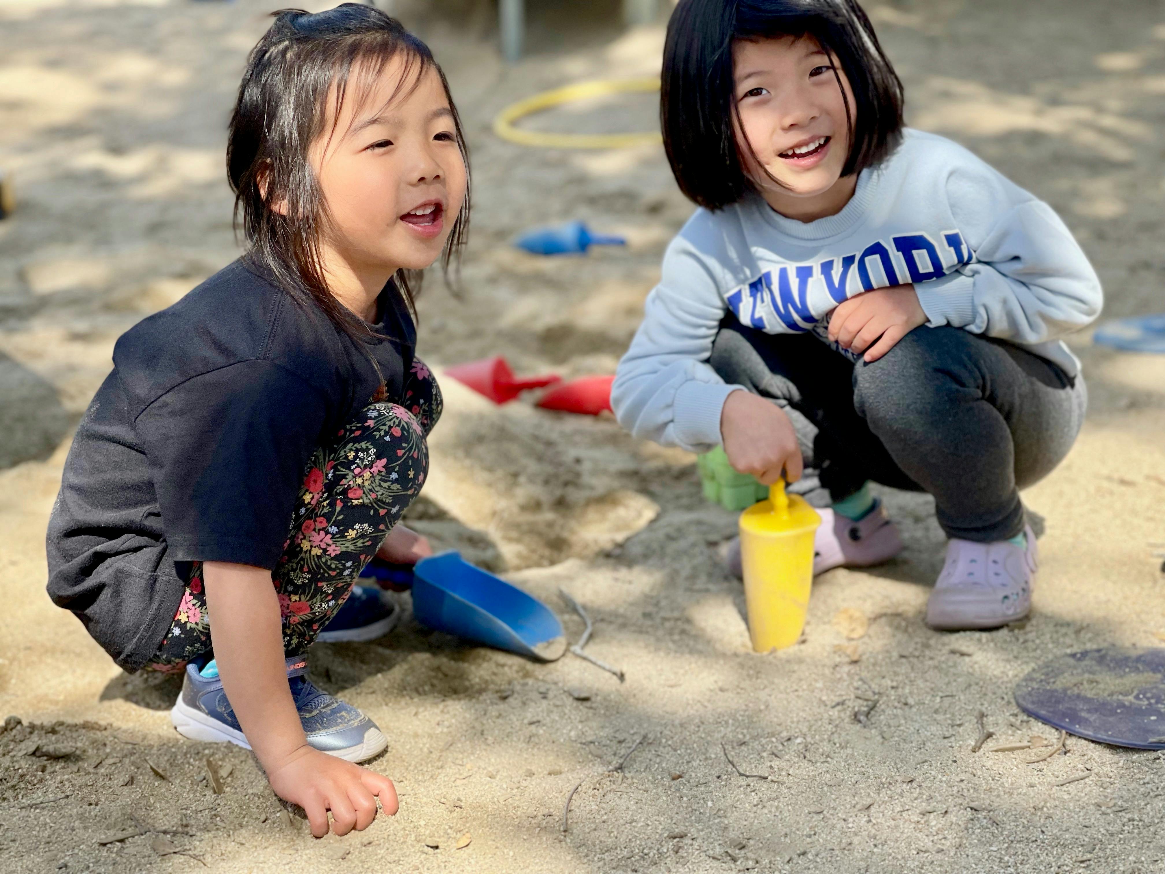 Two children playing in sand with shovels and cups