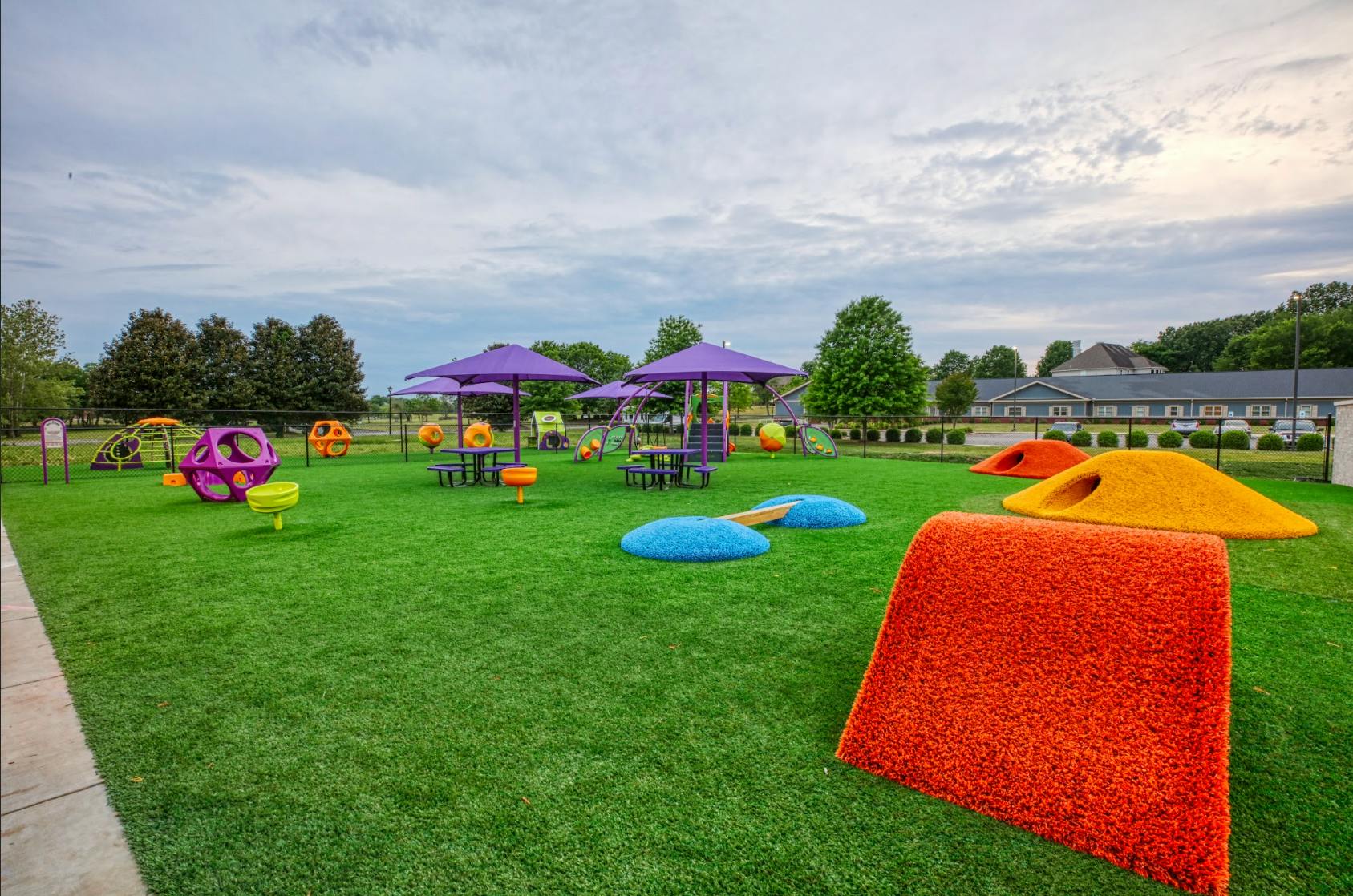 Outdoor play area with green turf, purple umbrellas, and colorful play structures