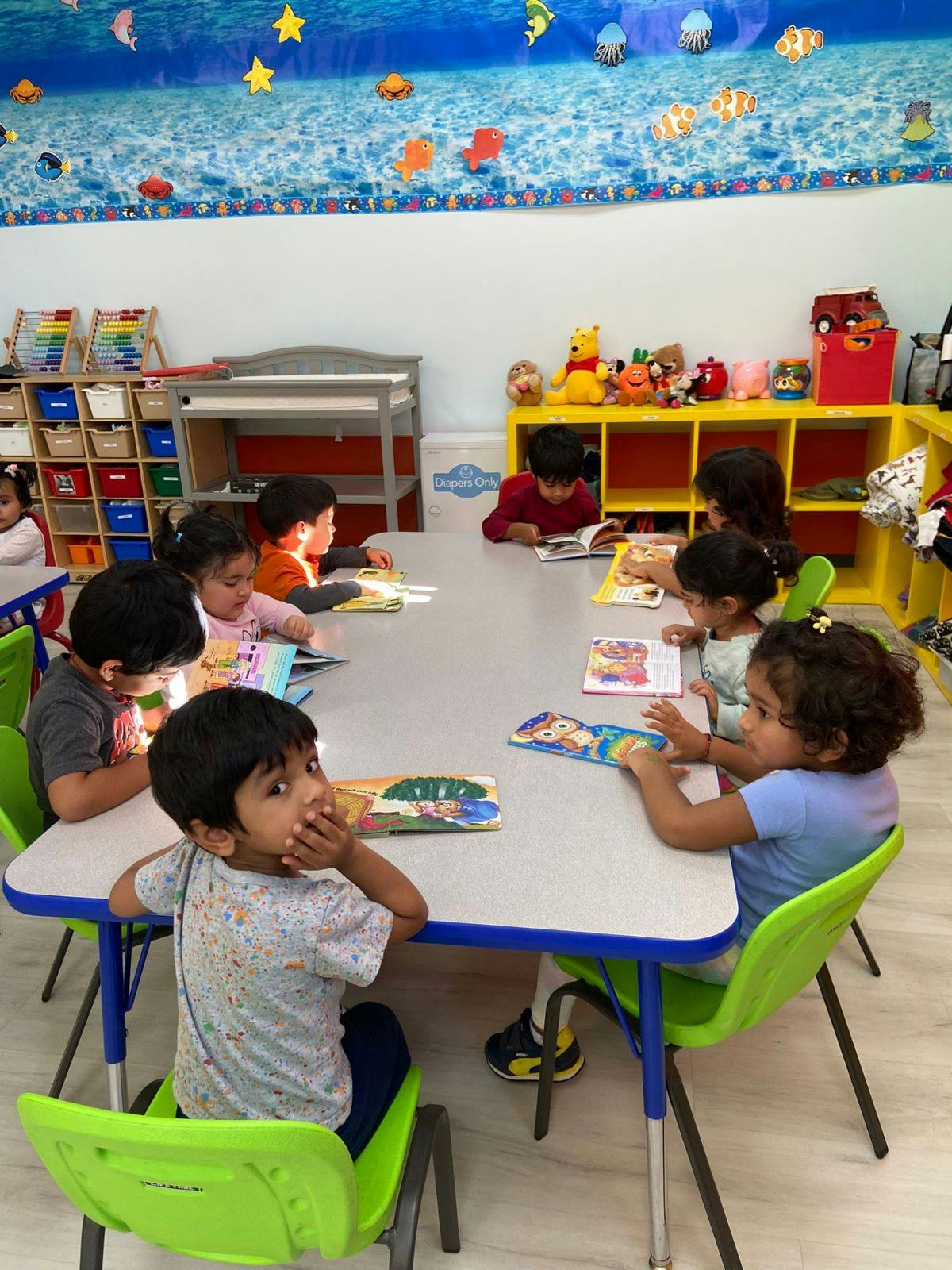 Children sitting at a table reading books in a classroom