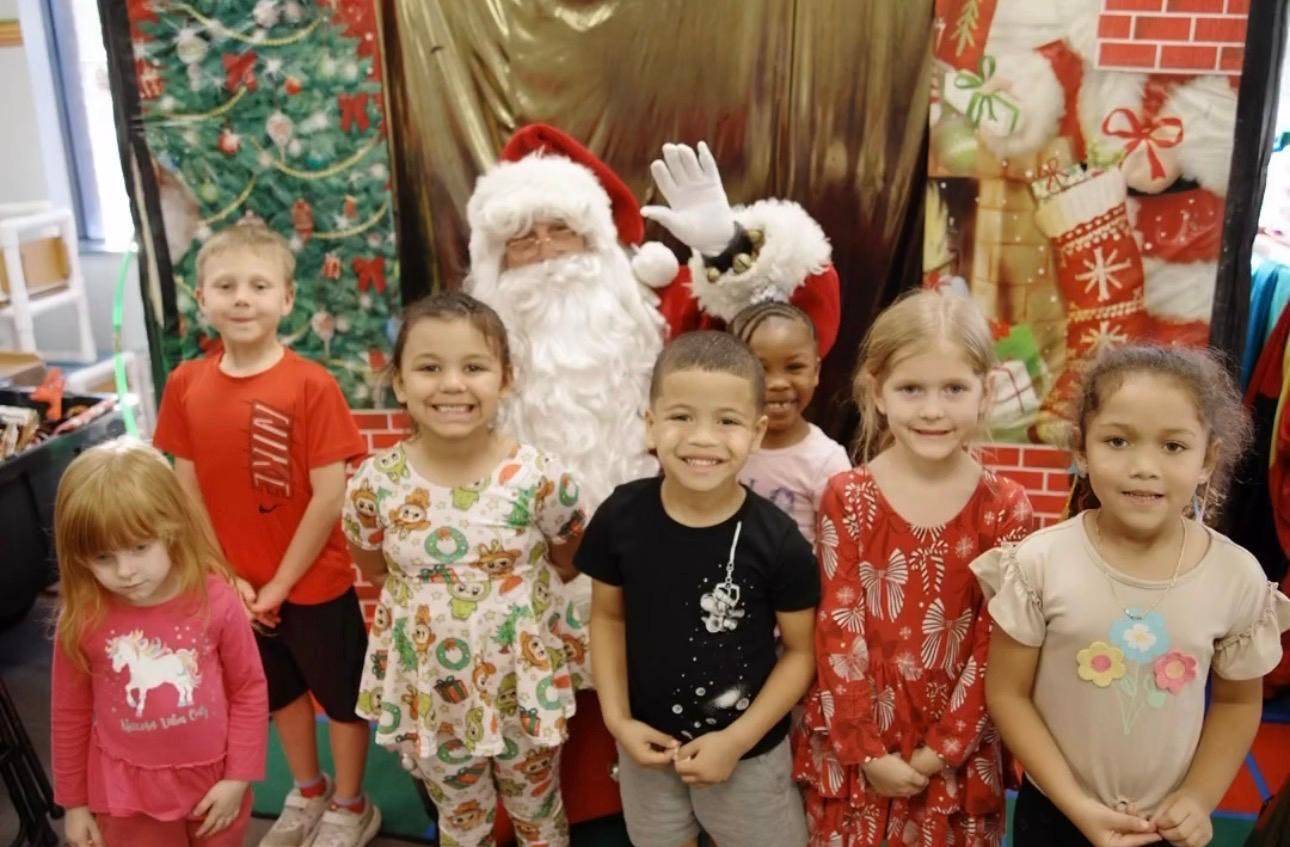 Group of children posing with Santa Claus in front of holiday decorations