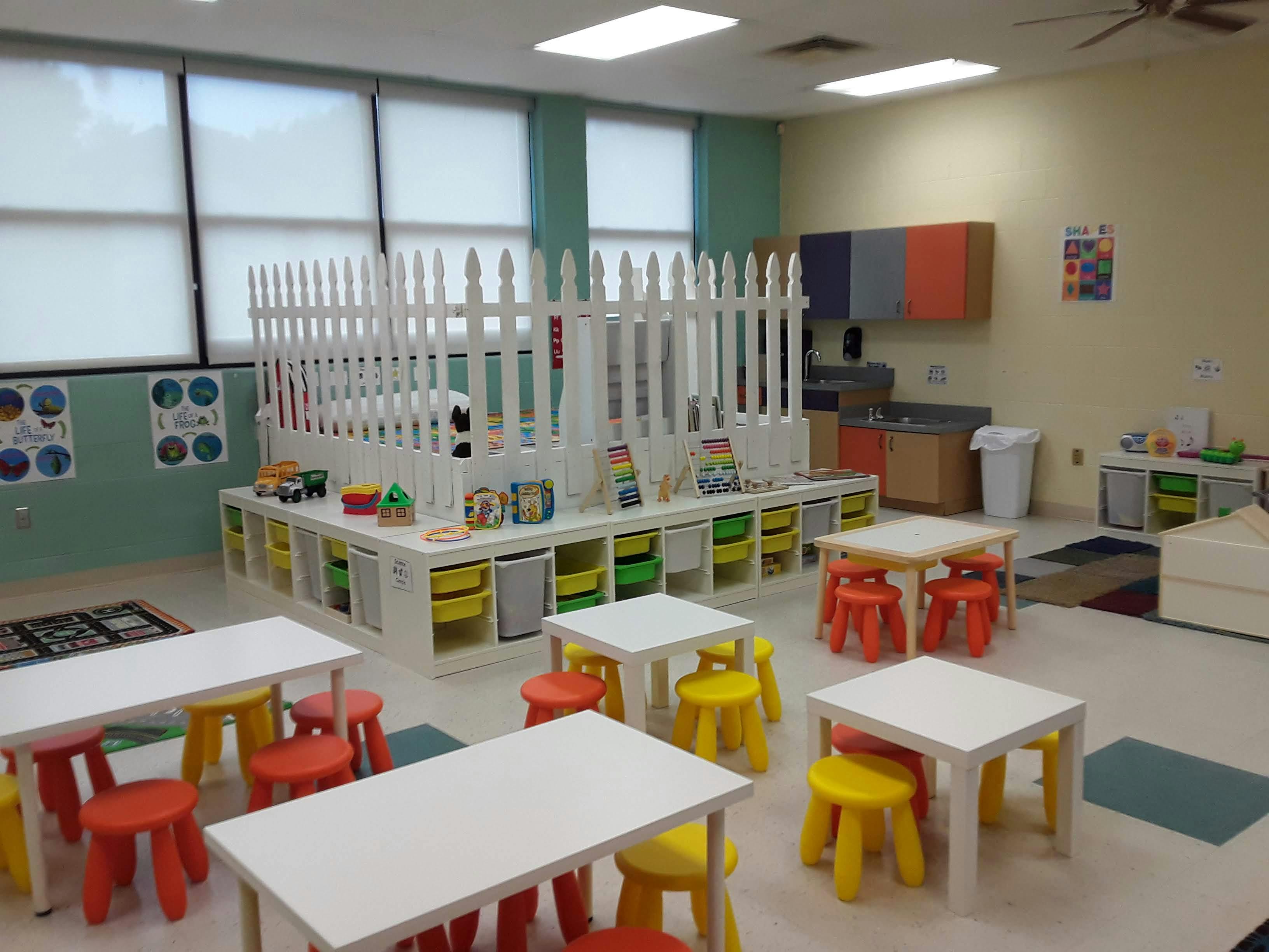 Classroom with small tables and chairs, and a play area with a white picket fence