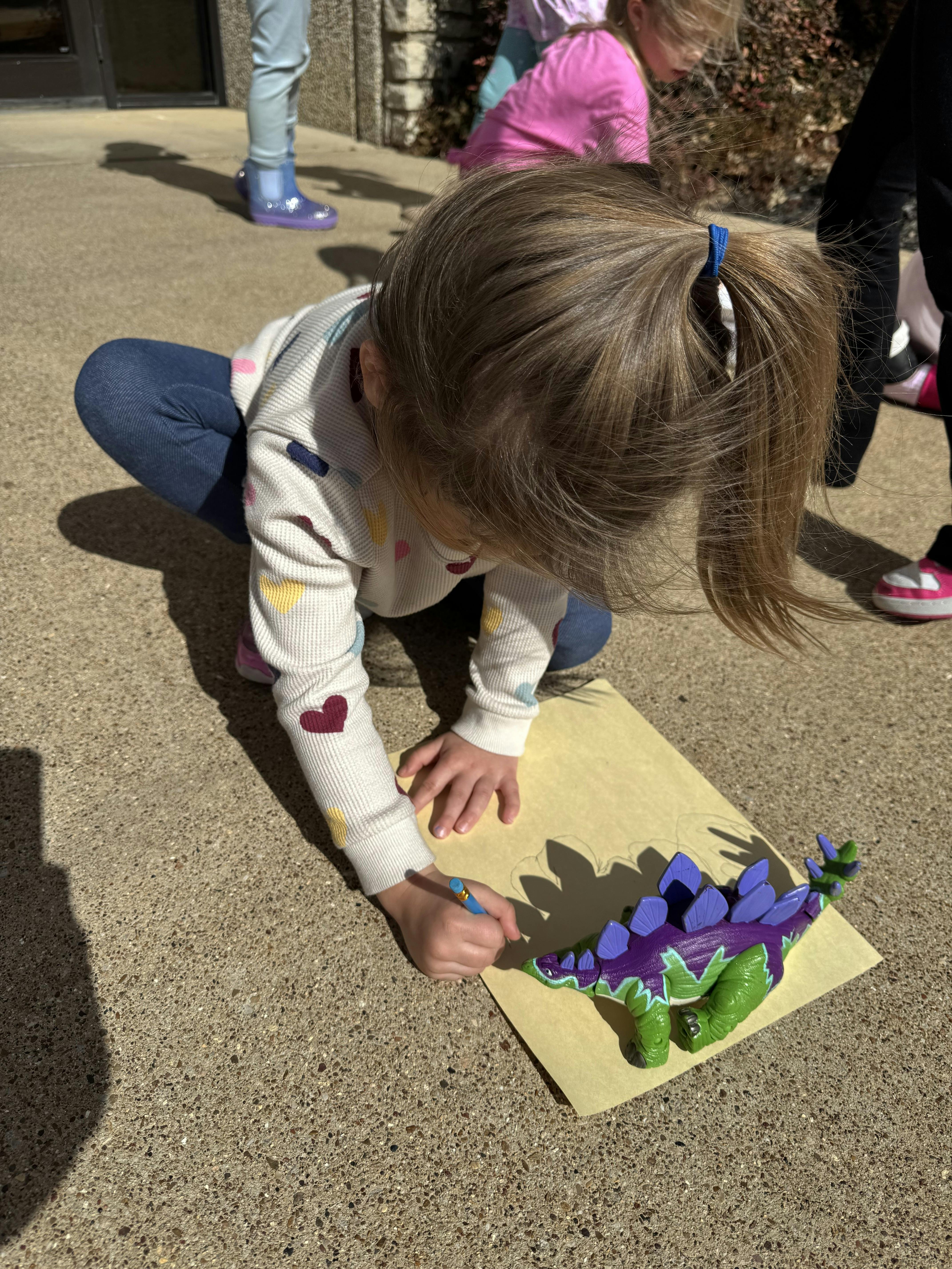 Child crouching, tracing a dinosaur toy onto paper