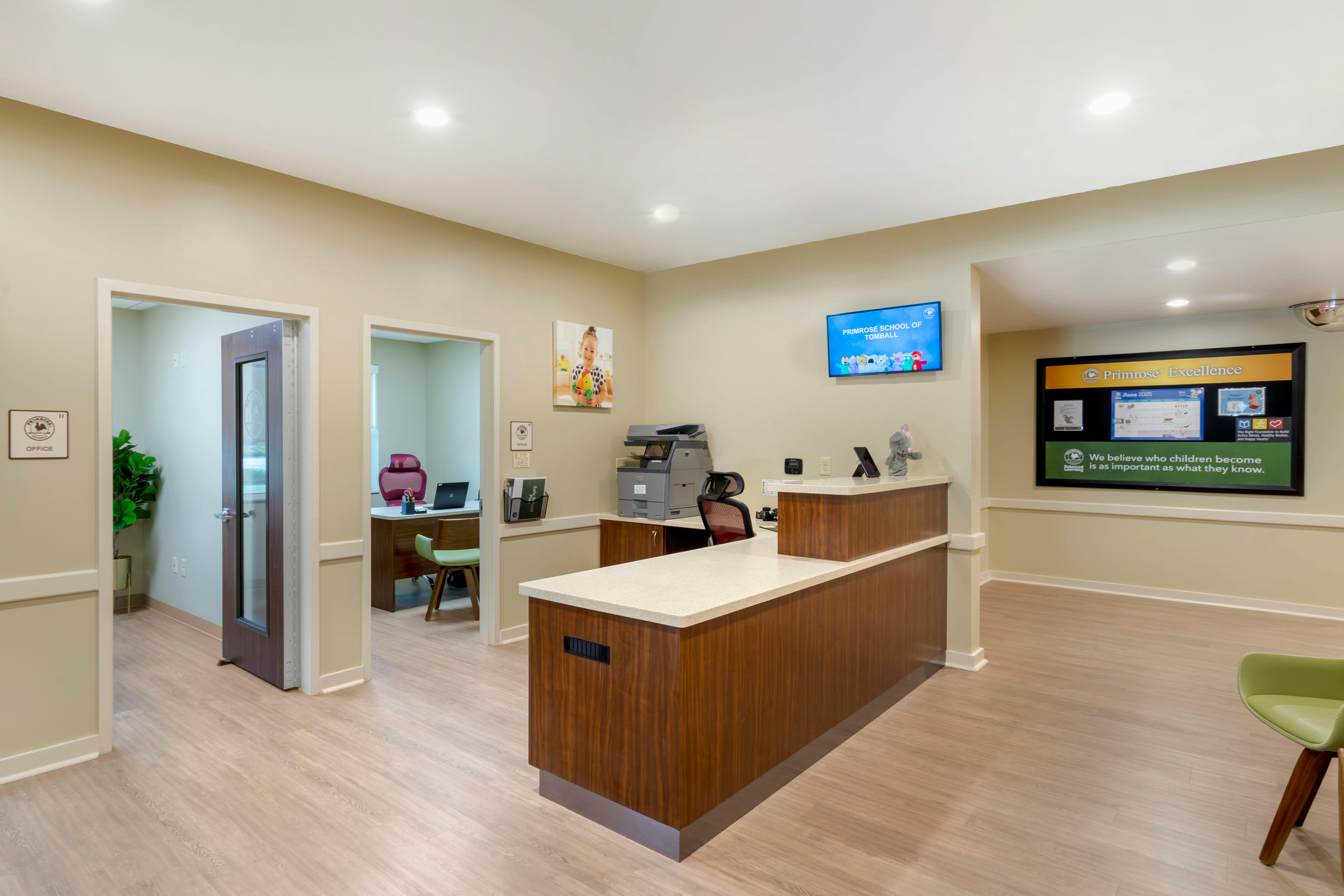reception desk in a lobby with office doors and a monitor displaying "Primrose School of Tomball"