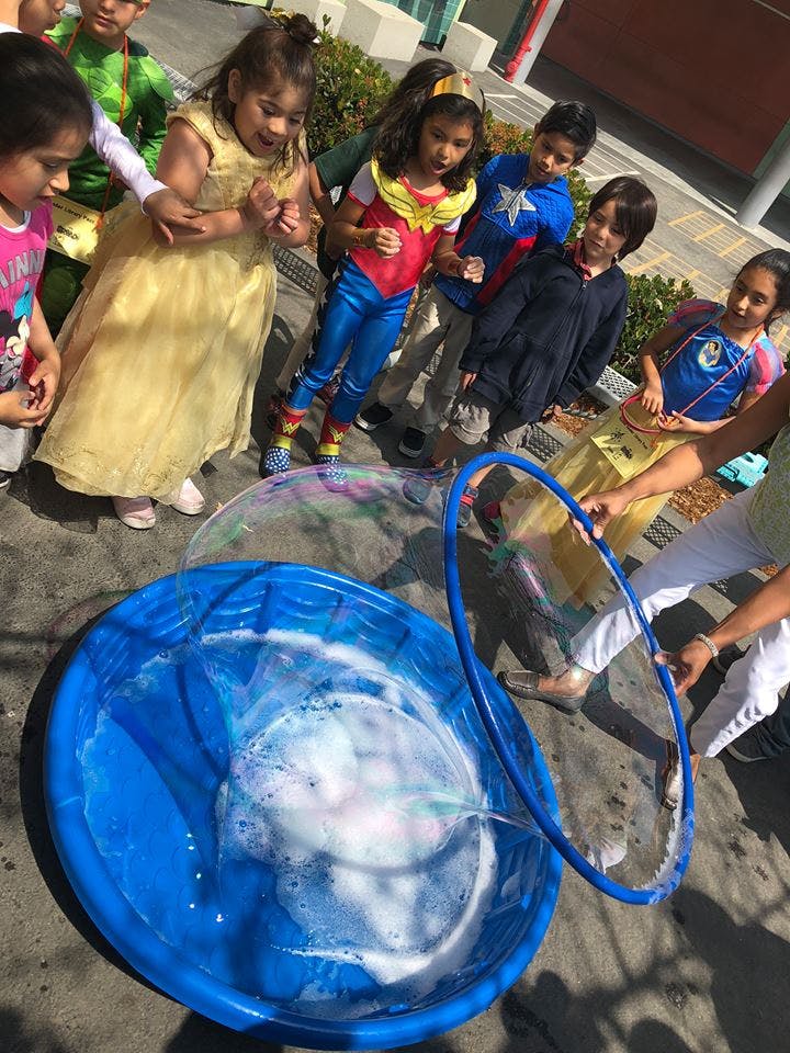 Children watching a person make a large bubble with a hoop and tub