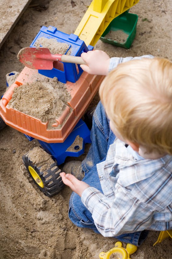 Child playing in sand with toy truck and shovel